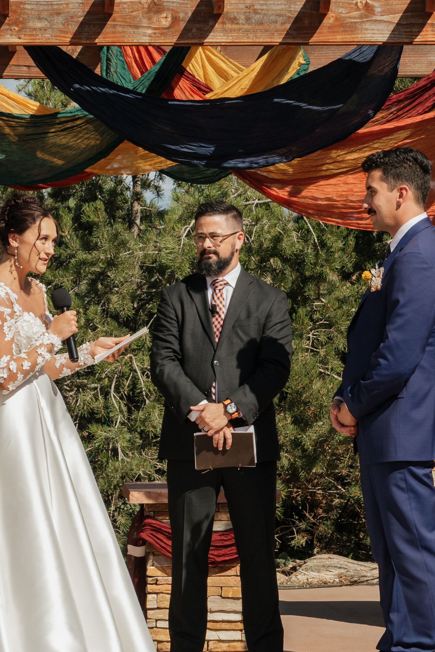 Outdoor wedding ceremony under a draped fabric canopy with wooden beams.