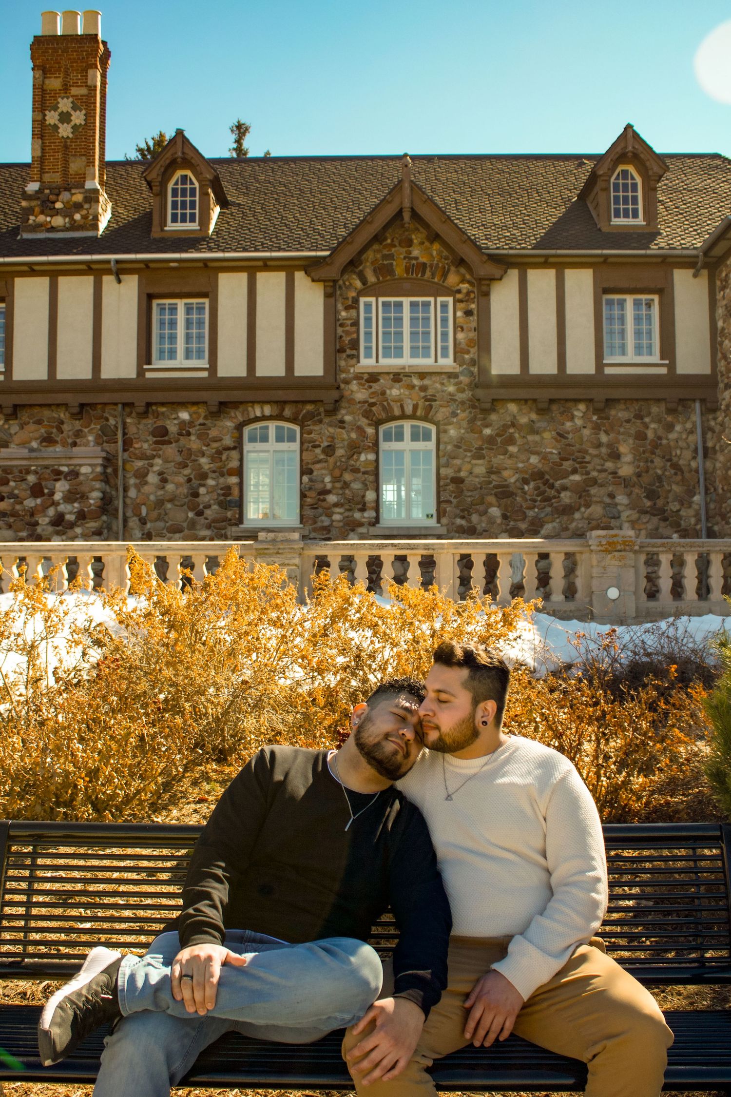 Two individuals share an affectionate moment on a bench surrounded by golden autumn foliage.
