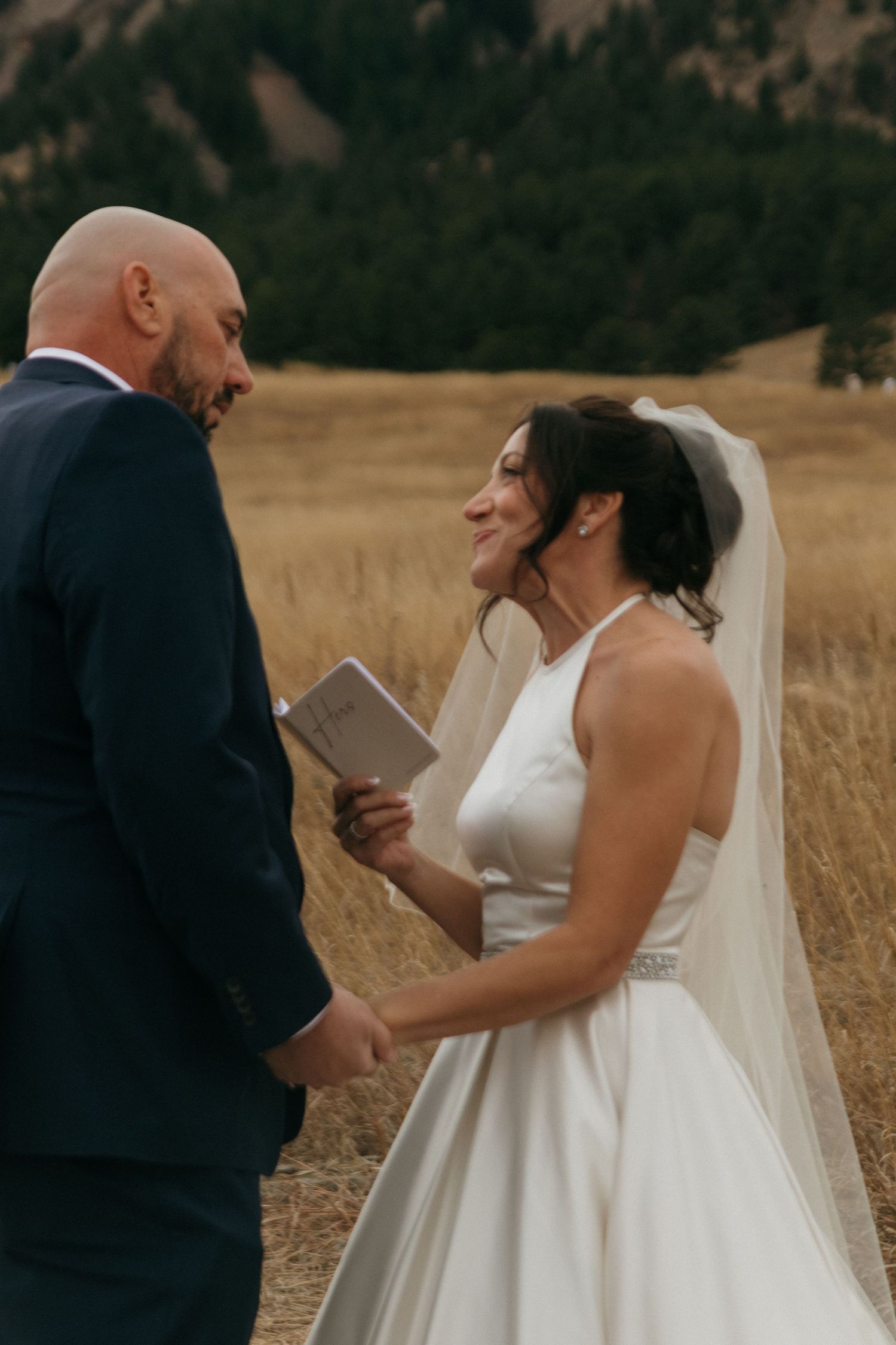 Couple exchanges vows in an outdoor ceremony against a backdrop of golden wheat fields.