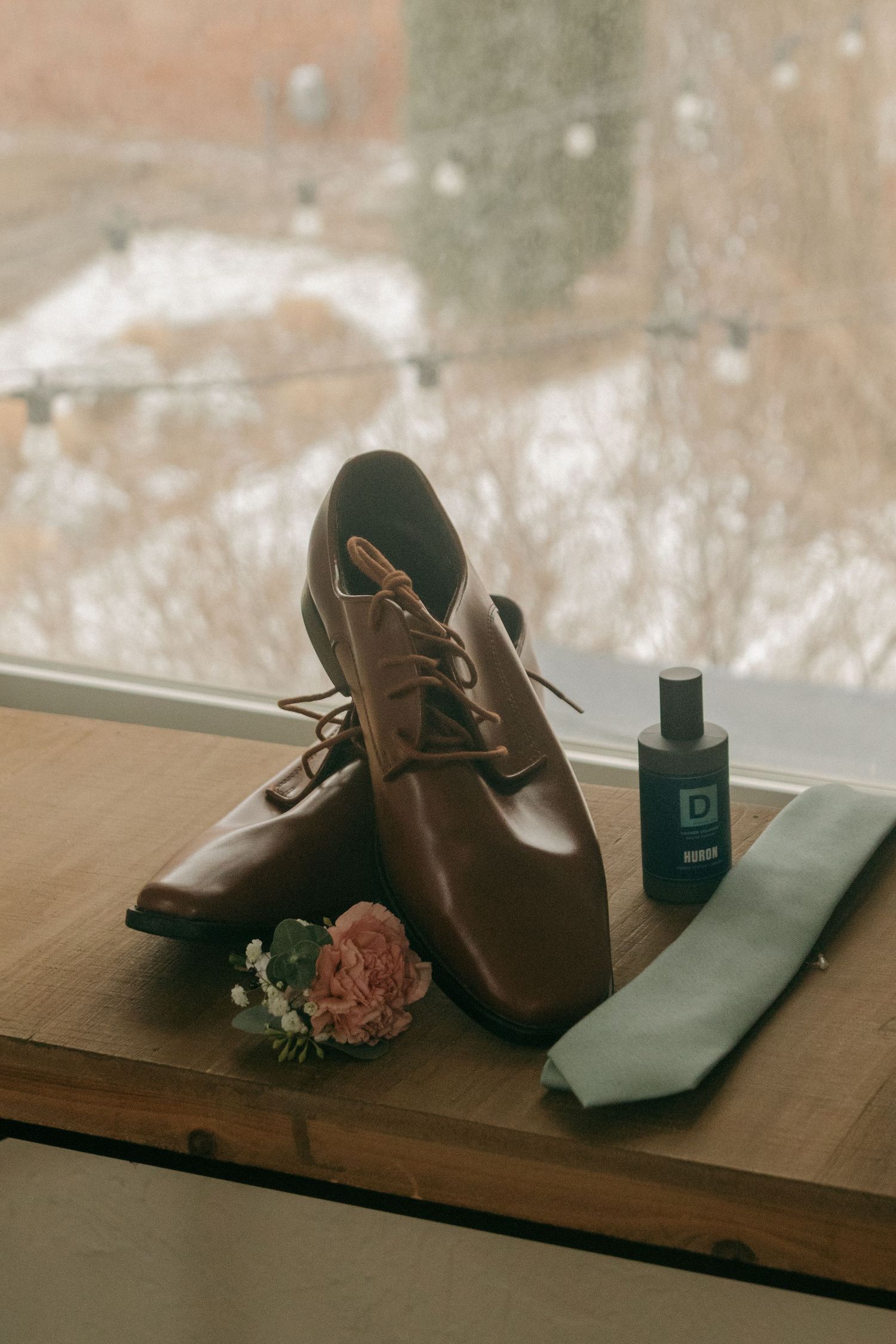 Brown leather shoes sit on a wooden surface with a dark wallet and small objects in warm vintage lighting.