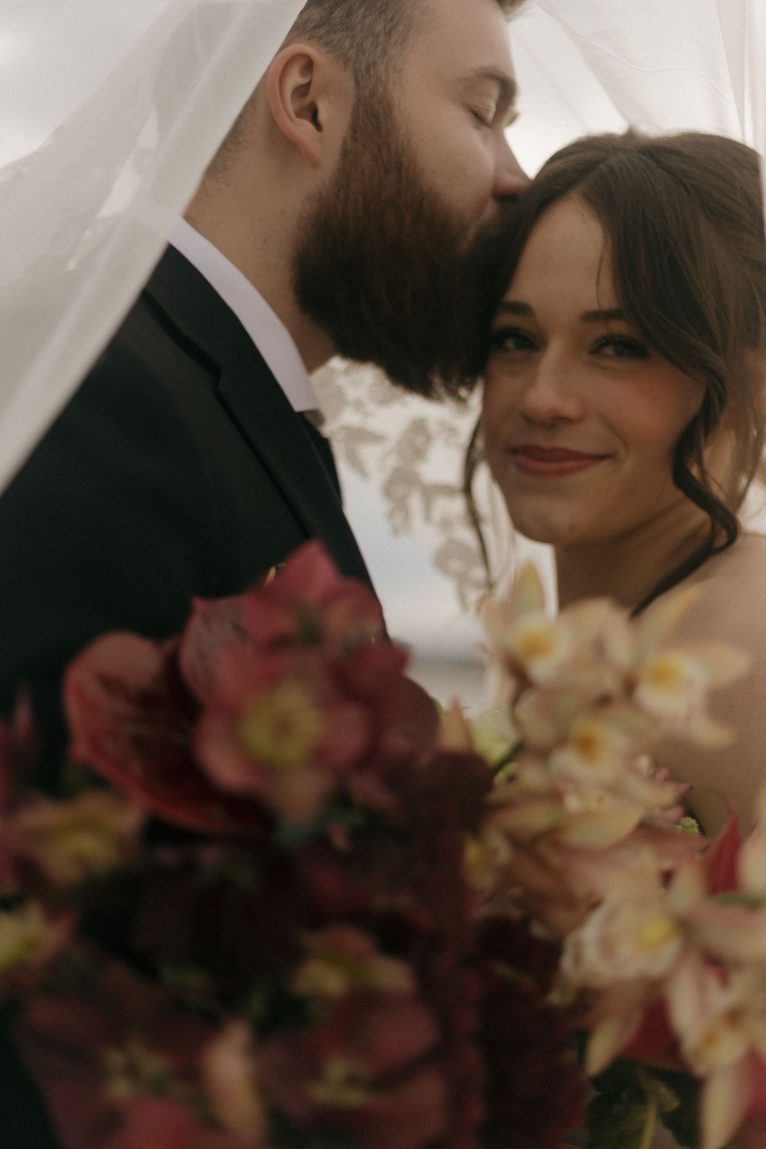 A romantic wedding couple embraces near blooming flowers in an intimate portrait.