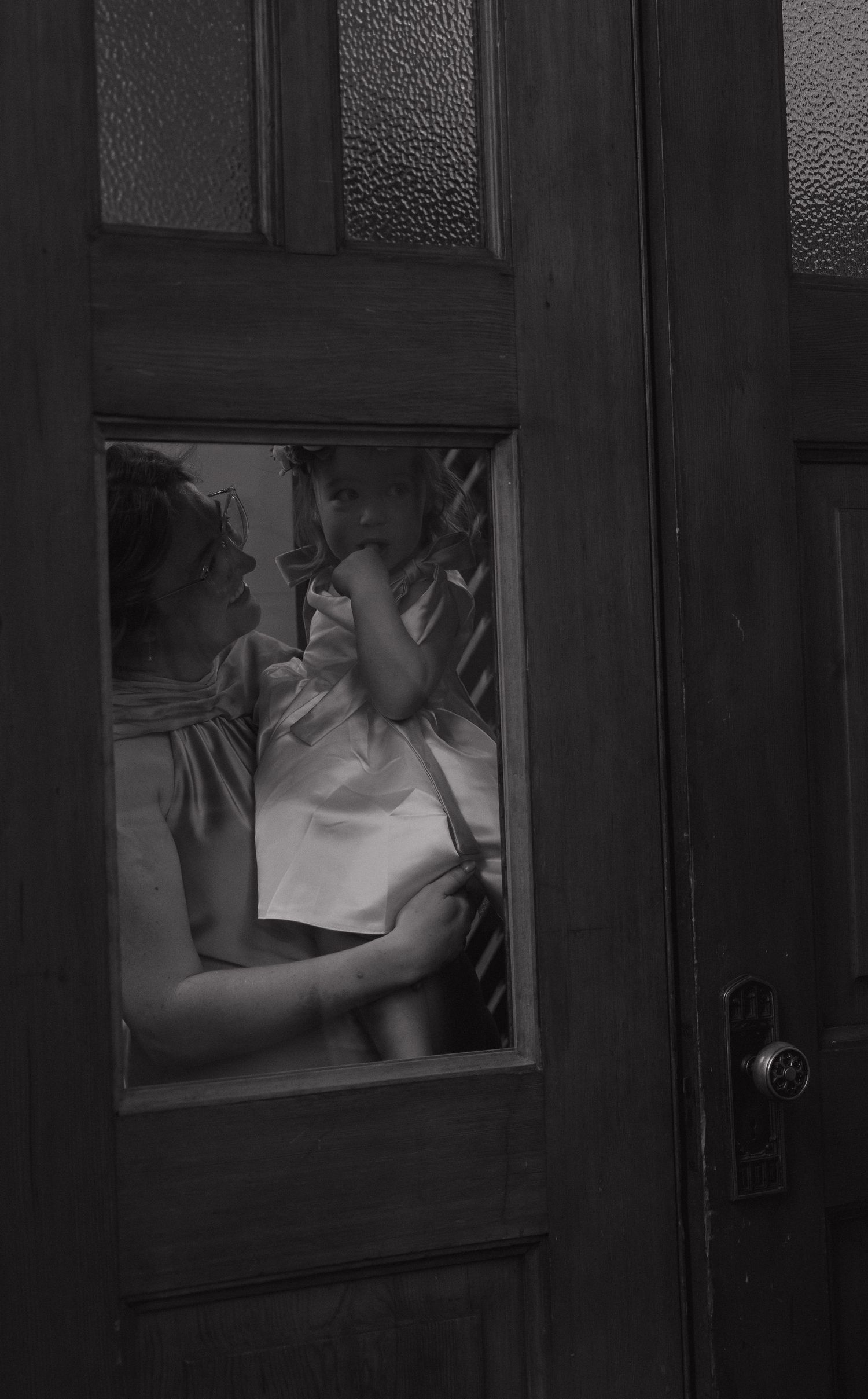 Black and white photo of two people embracing seen through a glass door window.