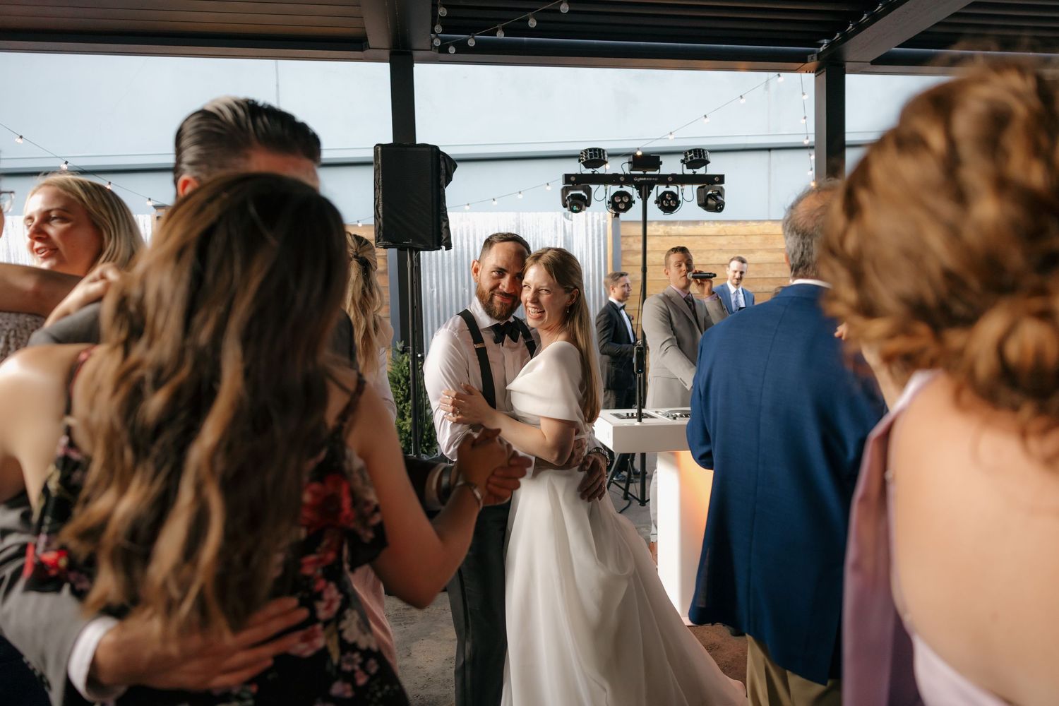 Newlywed couple embraces on the dance floor surrounded by celebrating guests at their wedding.