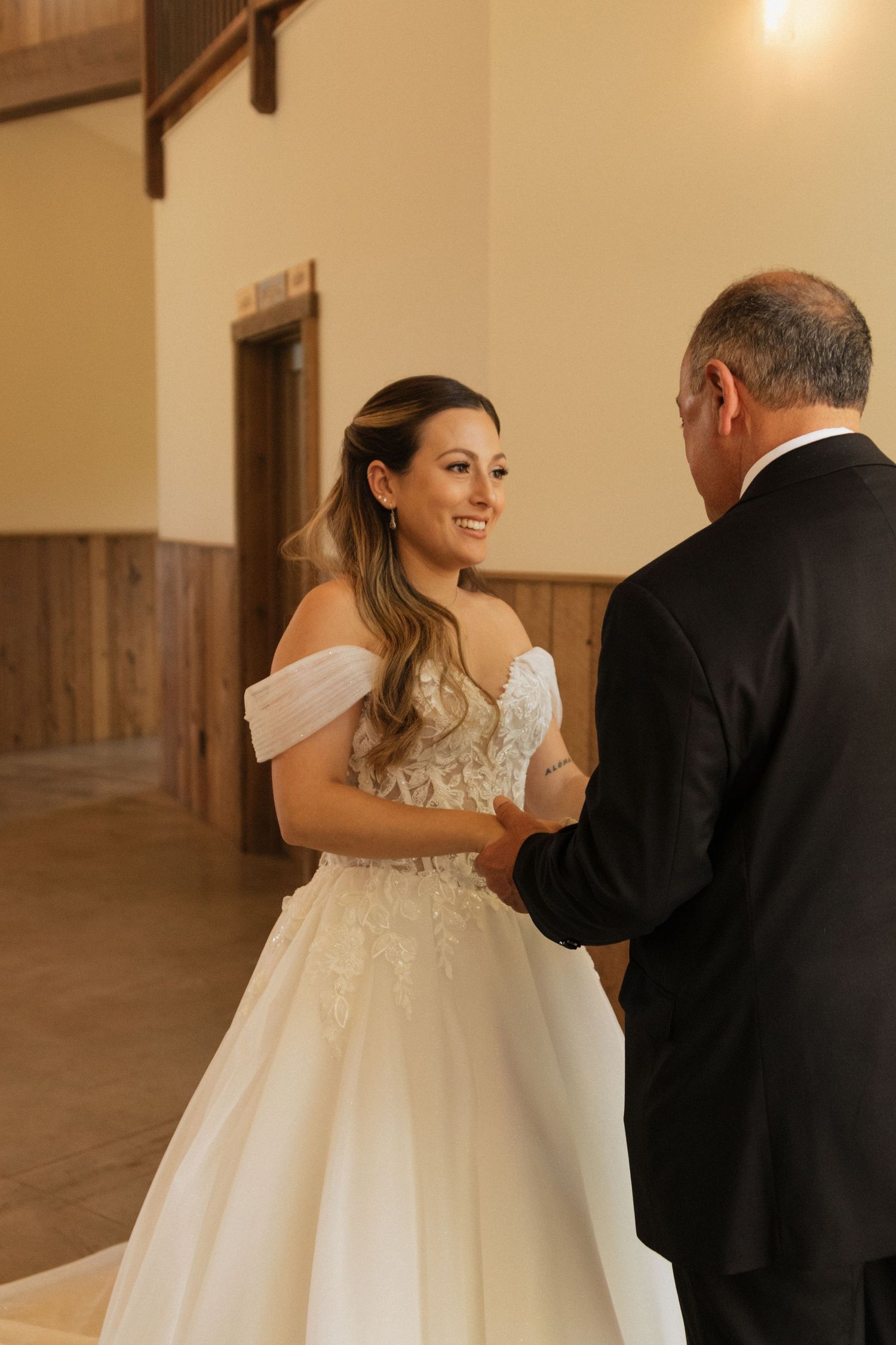 Bride in lace gown shares emotional first look with loved one in warm indoor setting.