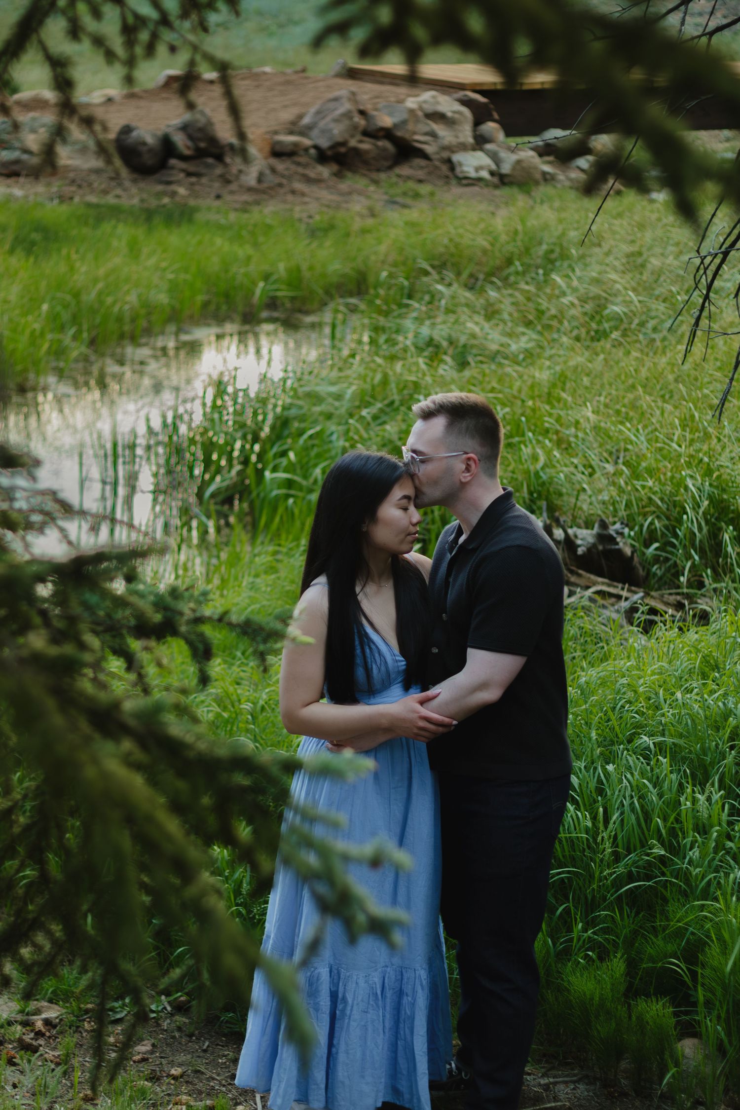 A romantic moment captured through tree branches near a small pond.