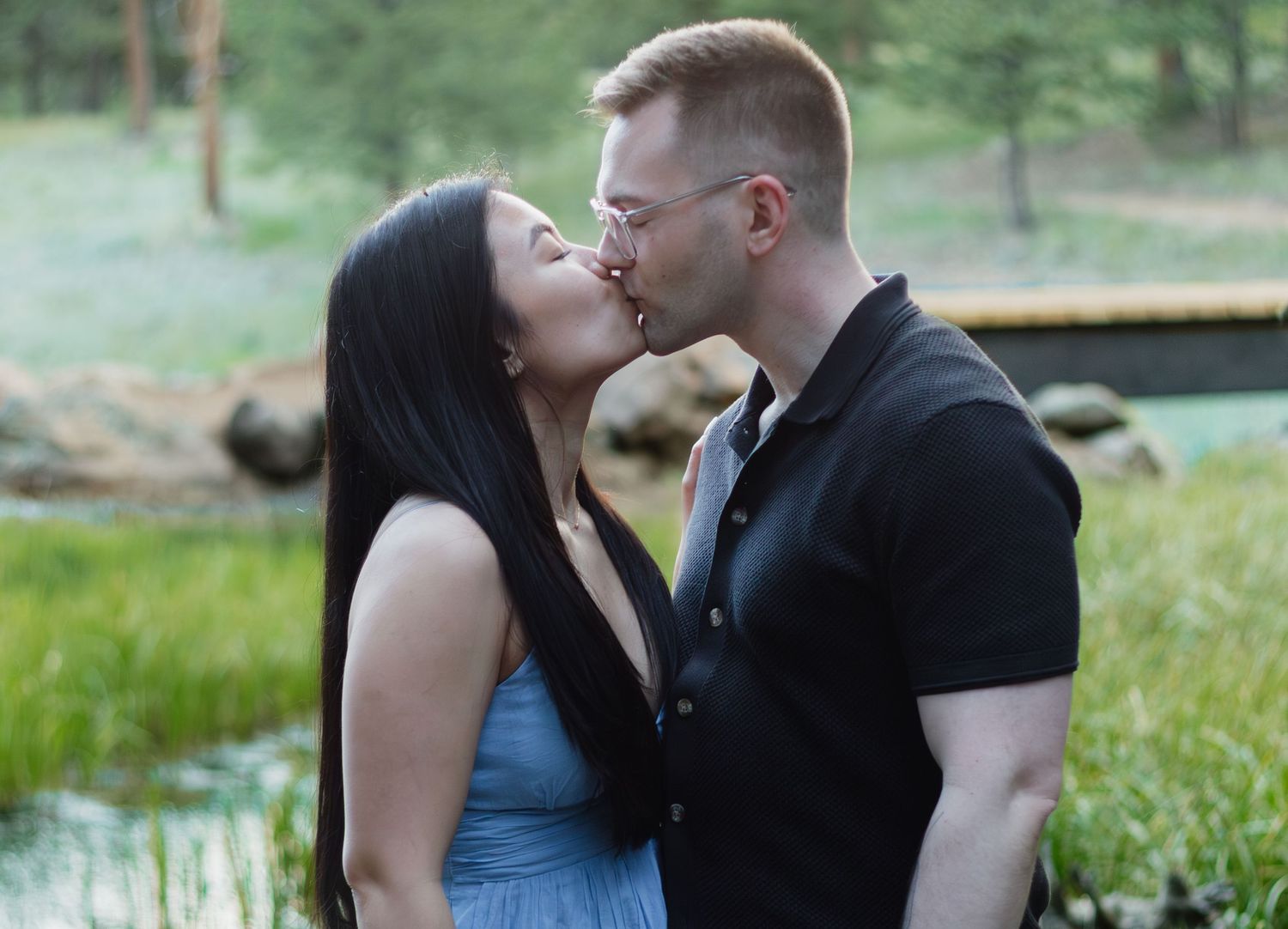 Tender moment shared between couple with blue dress against natural forest background.