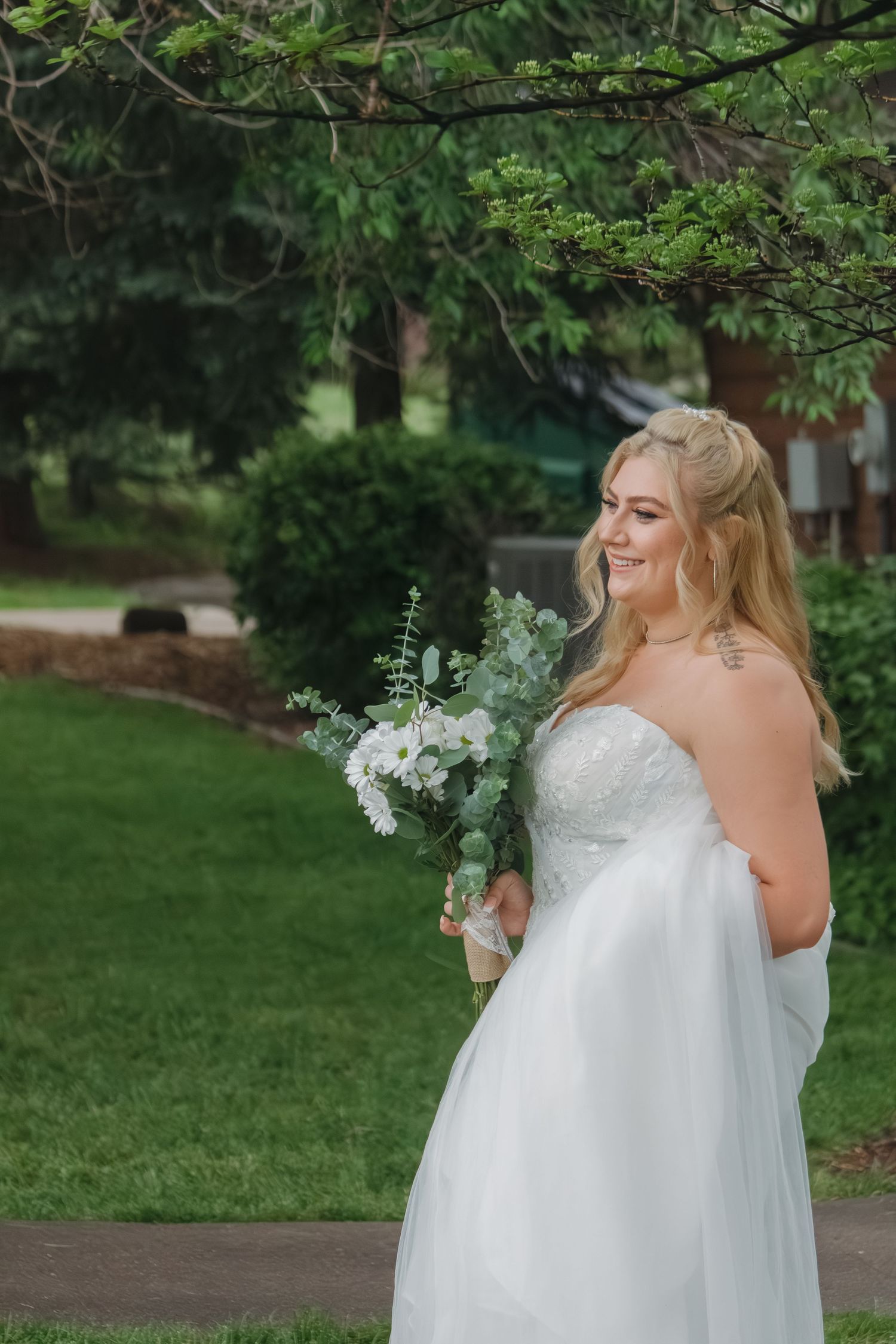 Bride in strapless white gown holding a bouquet of white and green flowers in garden setting.