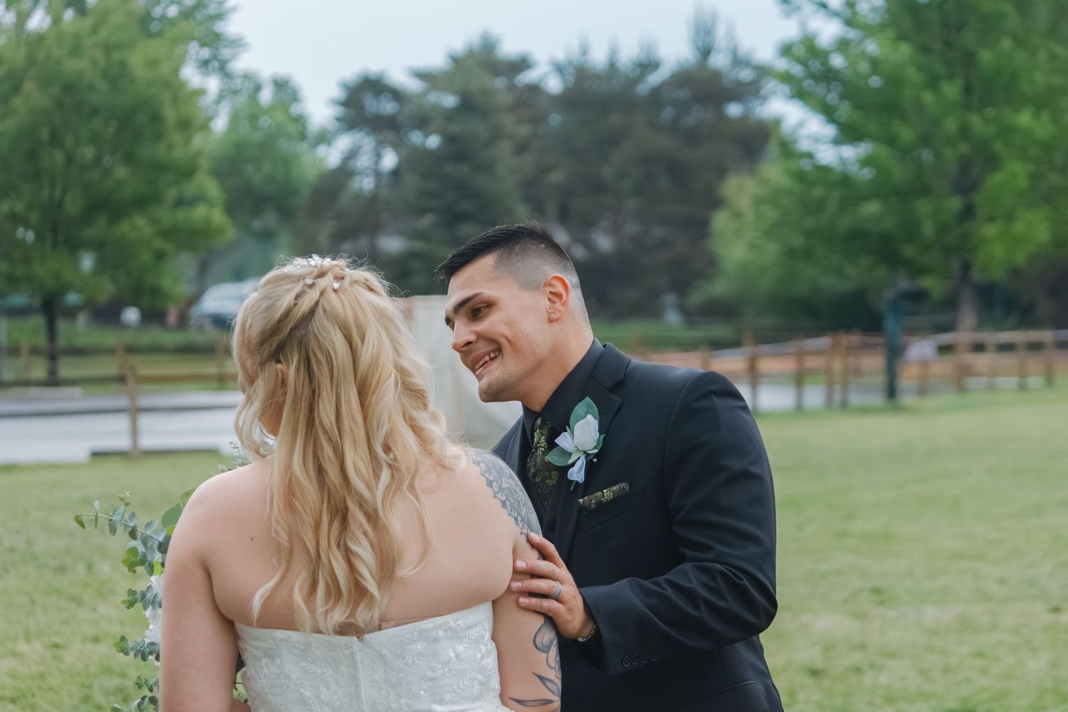 A romantic outdoor wedding moment between a bride in white and groom in black on a grassy field.