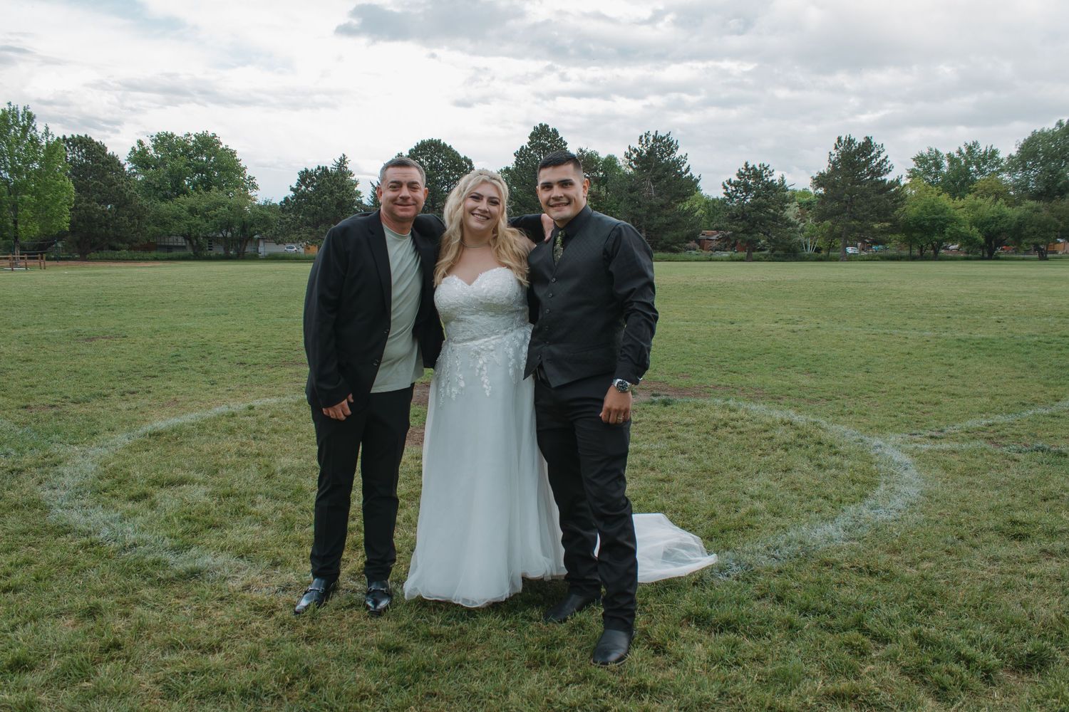 A small group gathers on a grassy field for photos under cloudy skies.