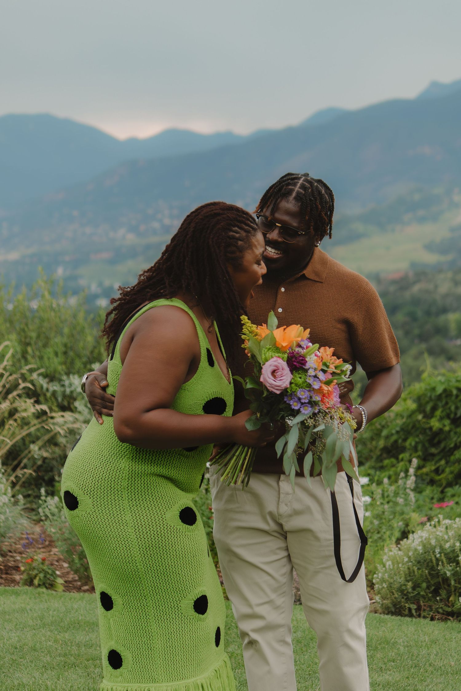 Romantic couple share tender moment in garden with mountain views and colorful bouquet.