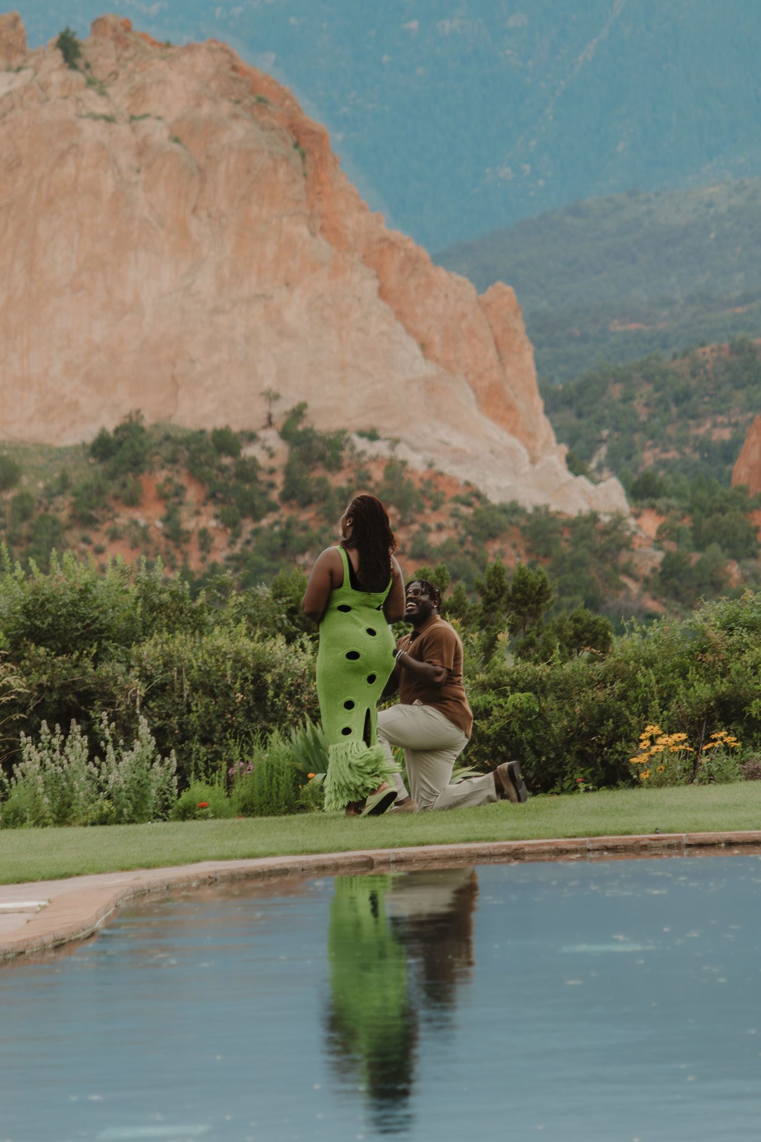 A couple enjoys a tranquil moment by a reflective pool with red rock formations at Garden of the Gods in the background.