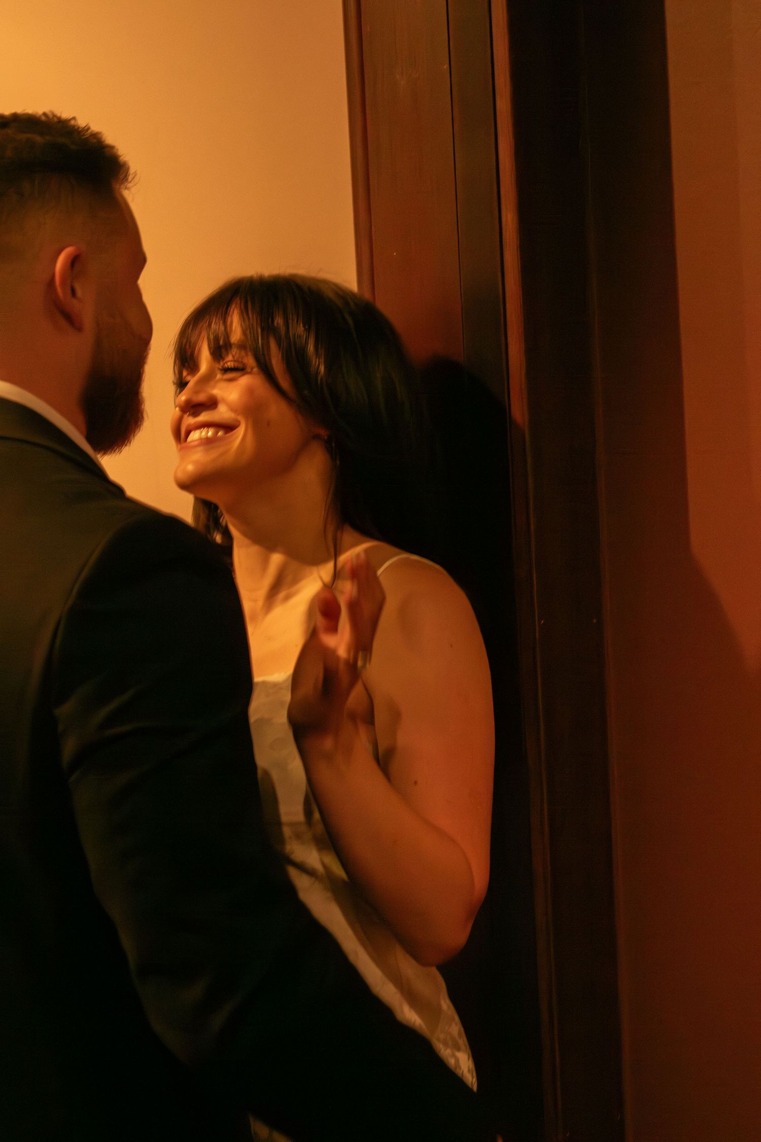 A couple shares an intimate moment against a warmly lit doorway.