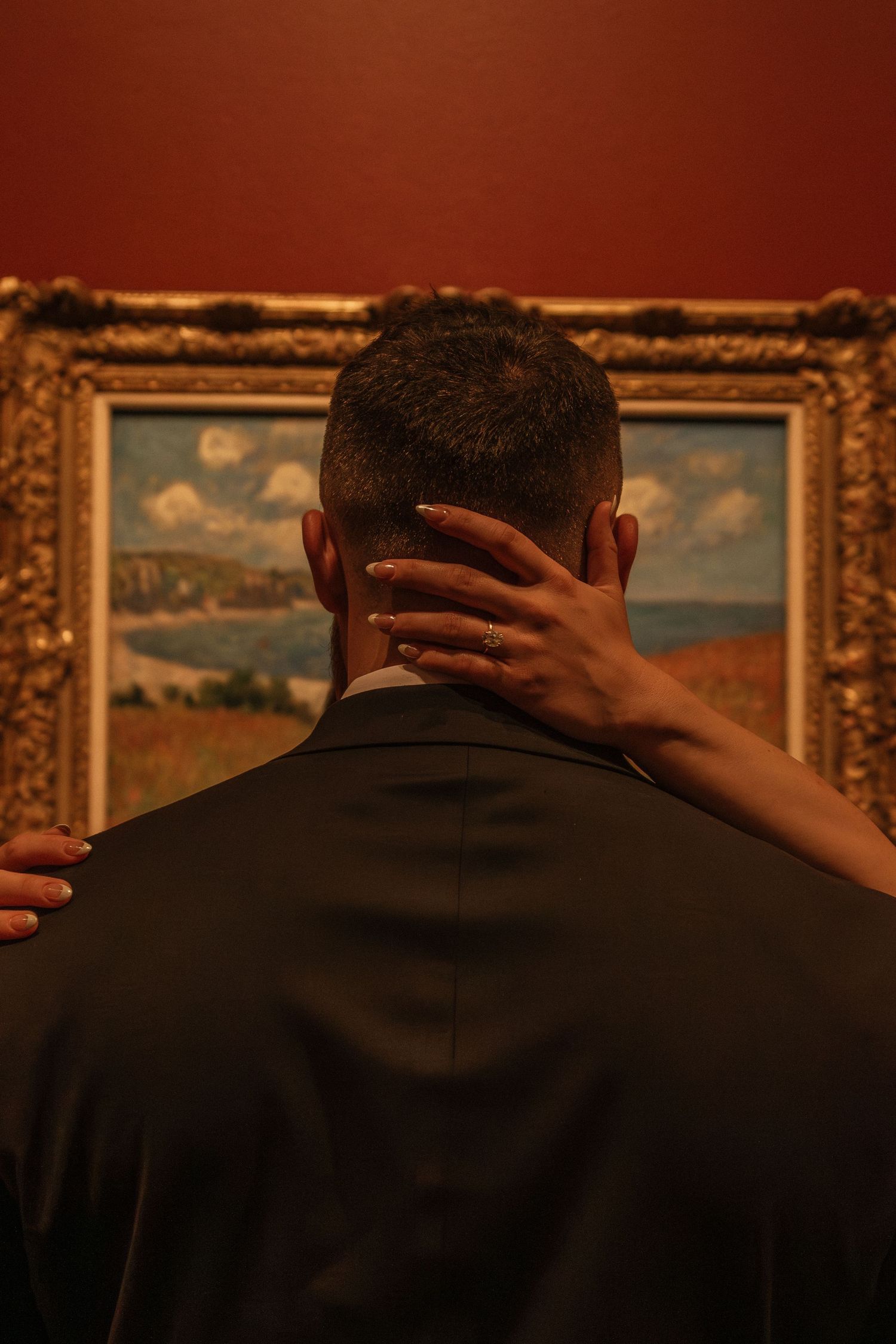 A silhouetted figure views a landscape painting in an ornate gold frame within a museum.