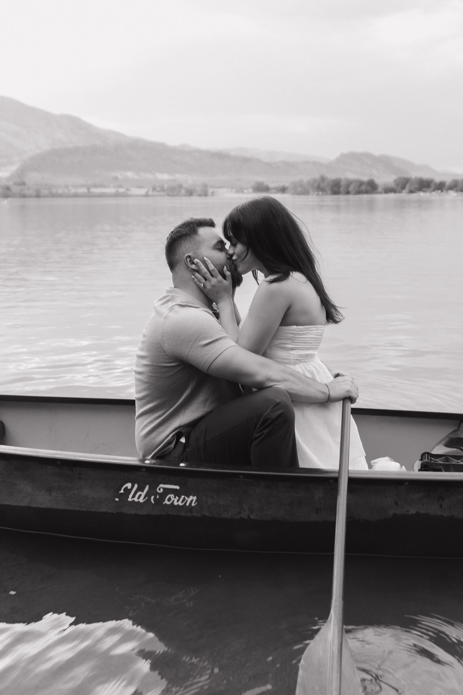 Romantic couple embracing in a boat on a serene lake with mountains in background.