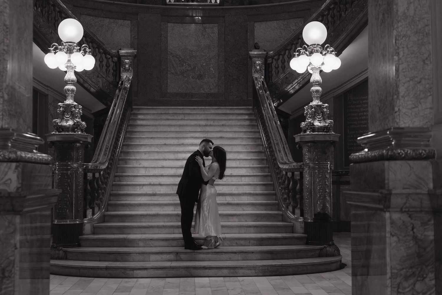 Black and white photograph of a grand staircase in an ornate historic building with elegant chandeliers and decor.