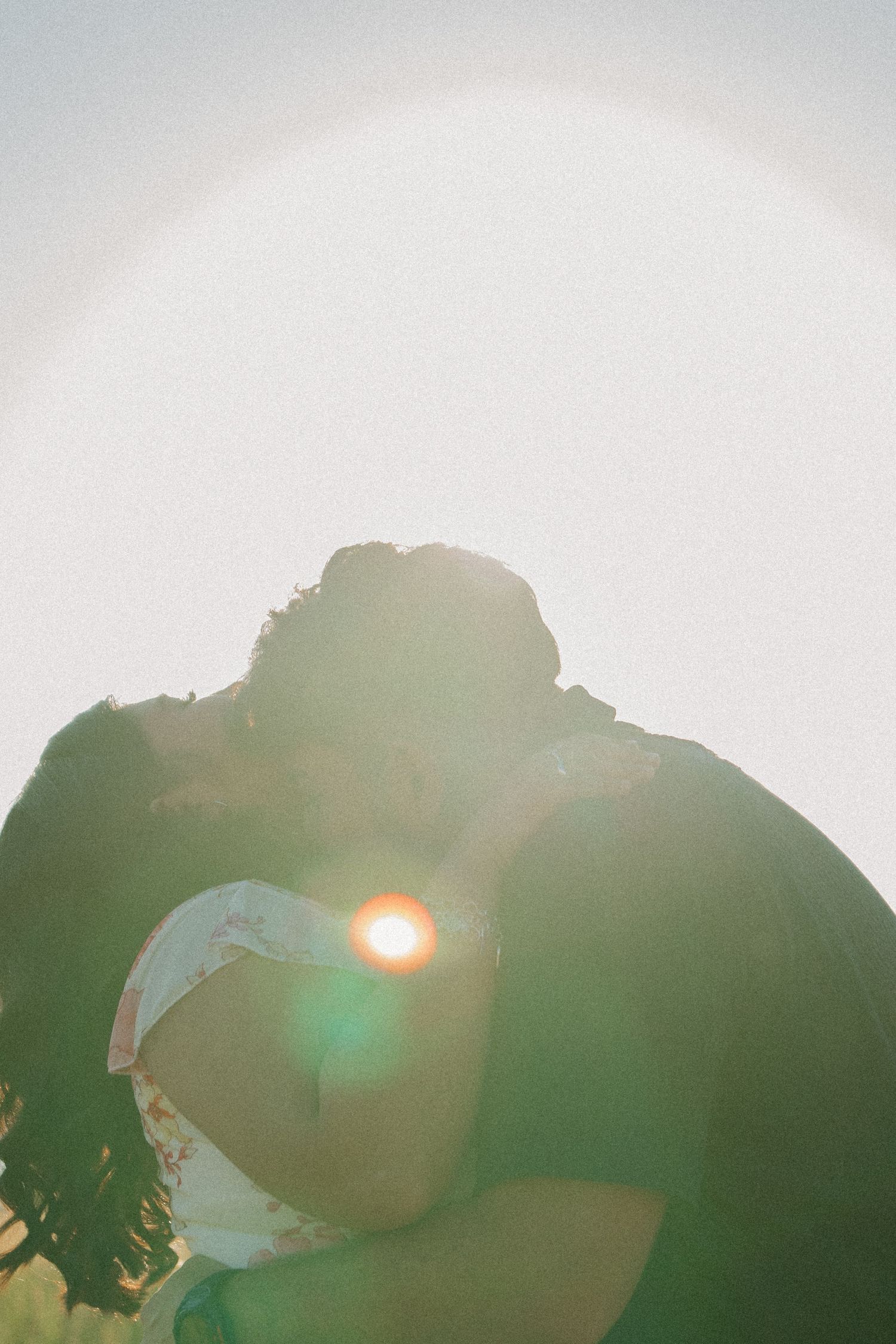 A silhouetted couple embraces against a bright sun creating a dreamy backlit effect.