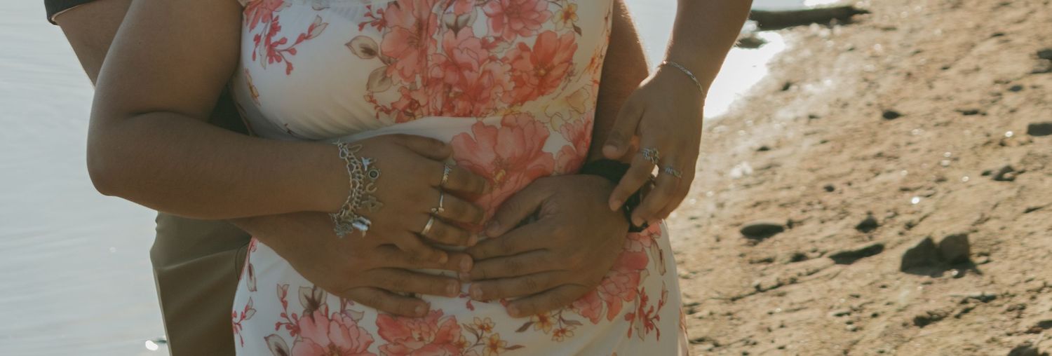 Close-up shot of hands resting together on a floral dress by the beach.
