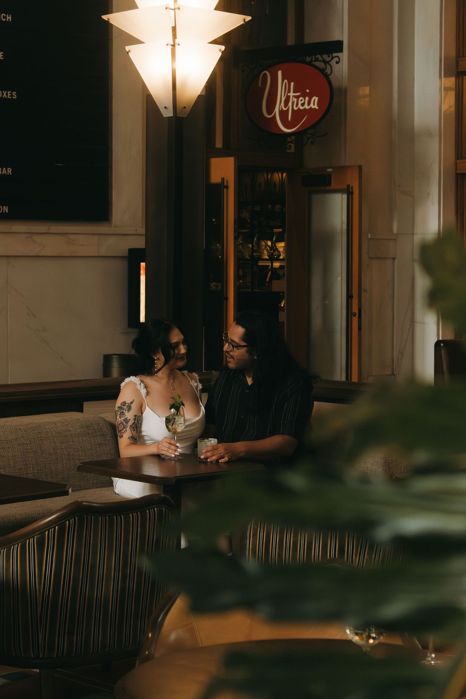 A romantic couple shares an intimate moment at a dimly lit restaurant with an illuminated fixture above.