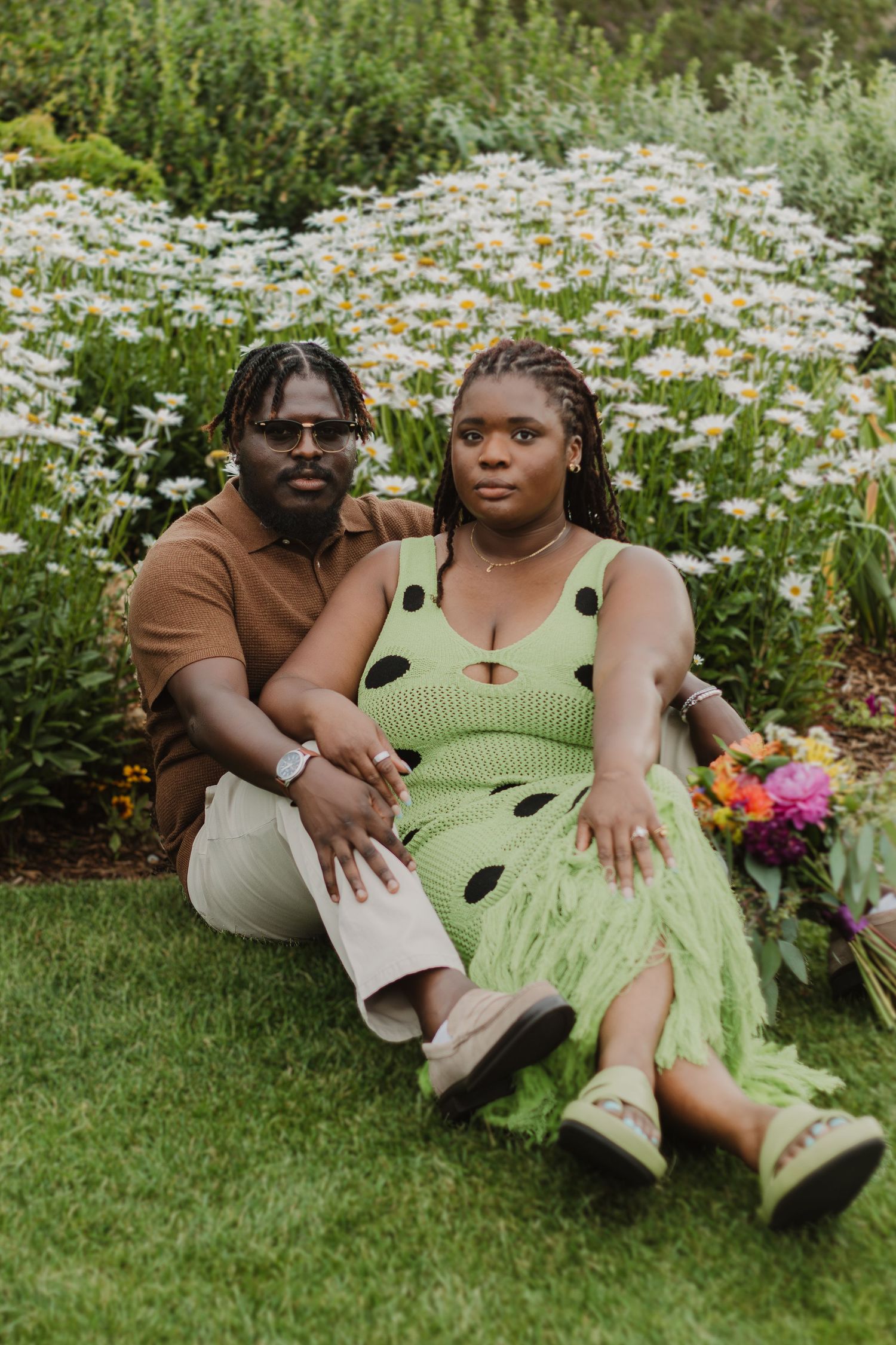A couple relaxes in a garden filled with blooming white daisies, wearing casual summer attire.