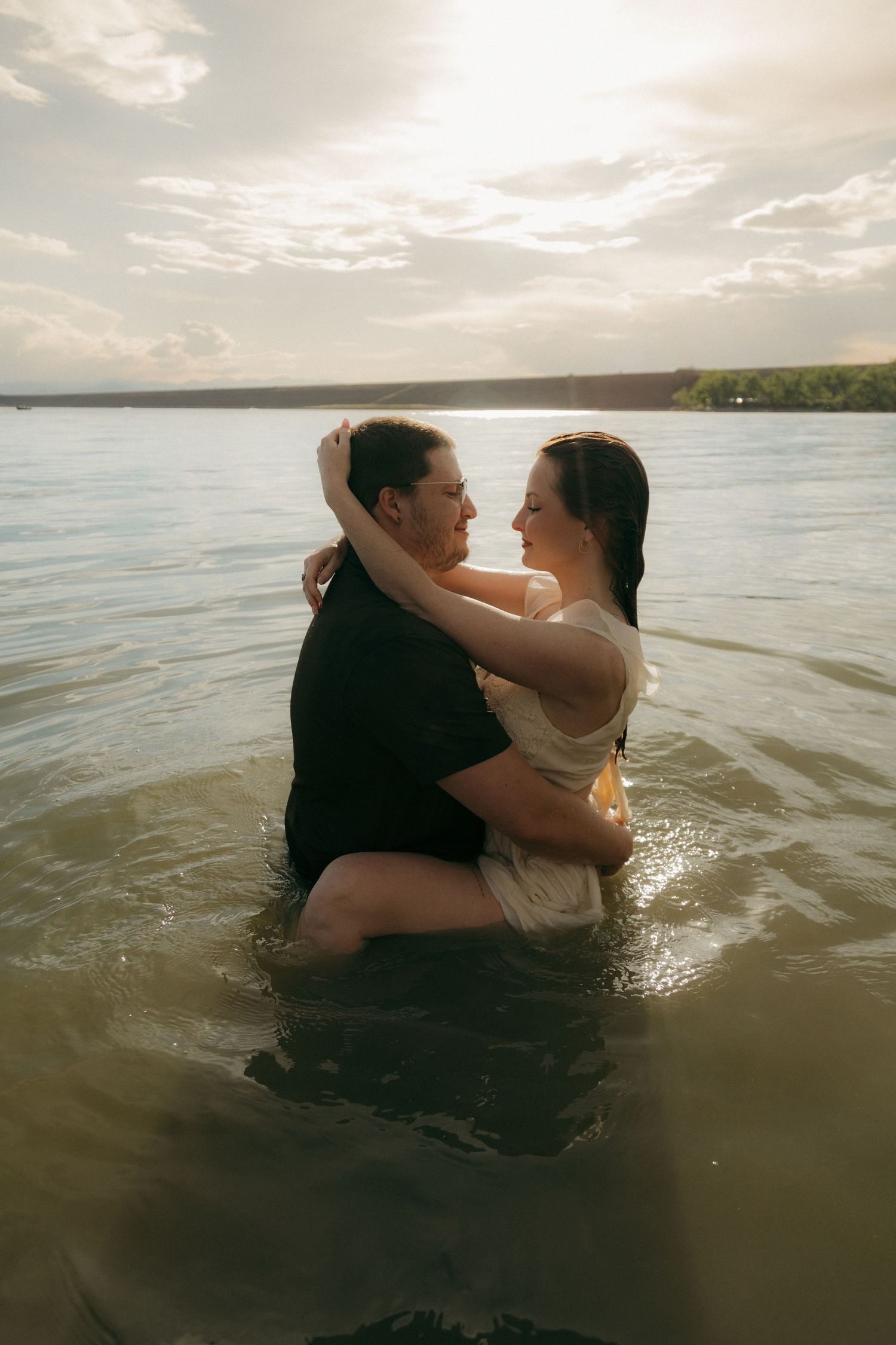 Couple embracing romantically while standing in a lake at golden hour sunset.