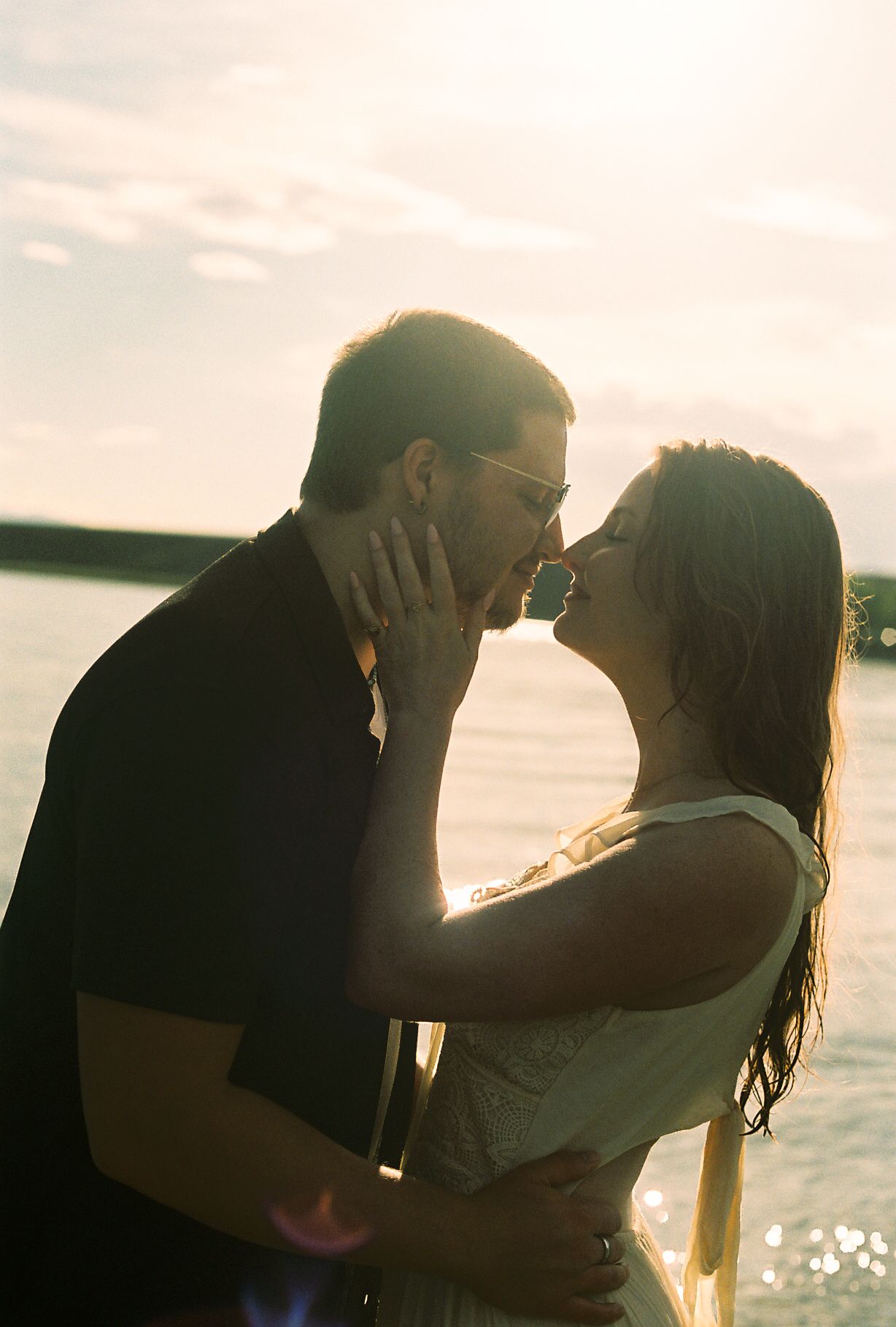 Couple kissing passionately backlit by stunning golden sunset light during lakeside photo session.