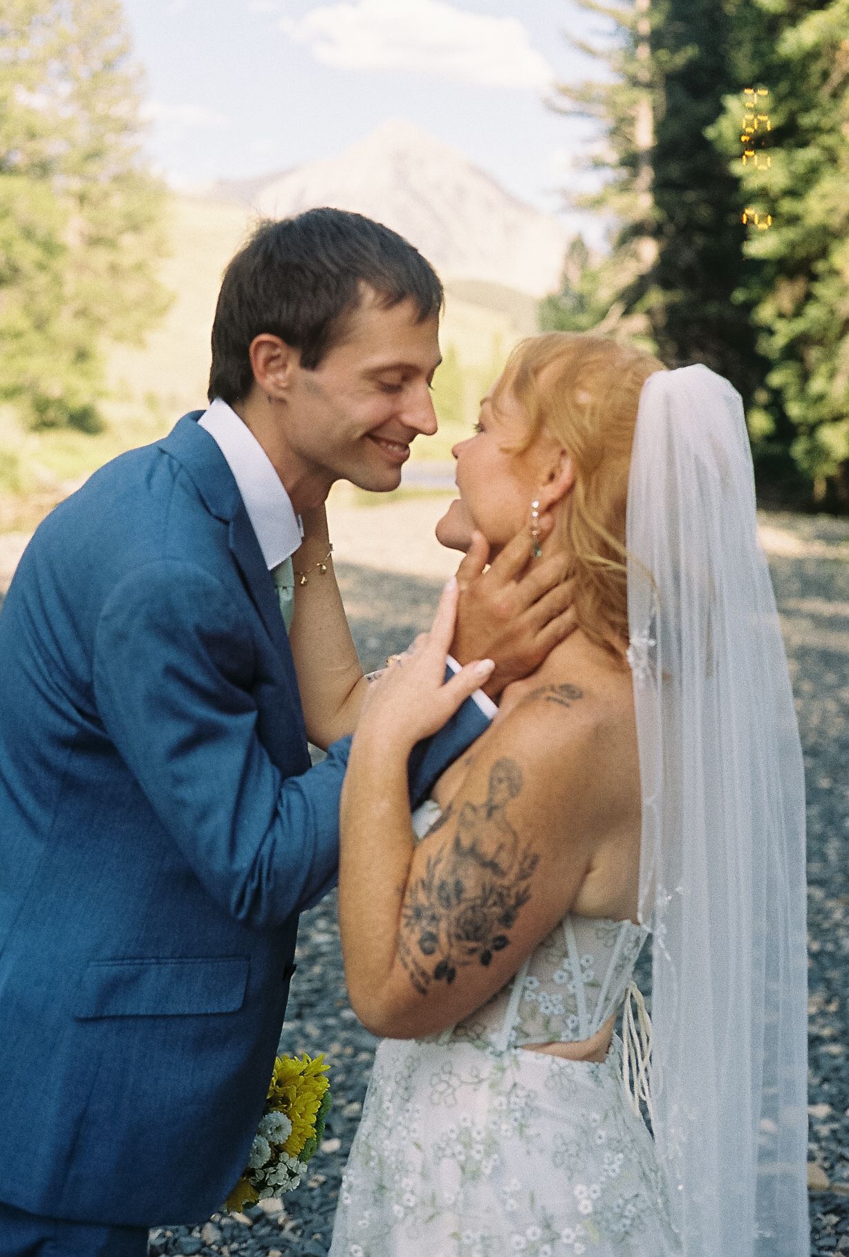 Groom in blue suit tenderly holds brides face as they share romantic moment, bride wearing lace wedding gown.