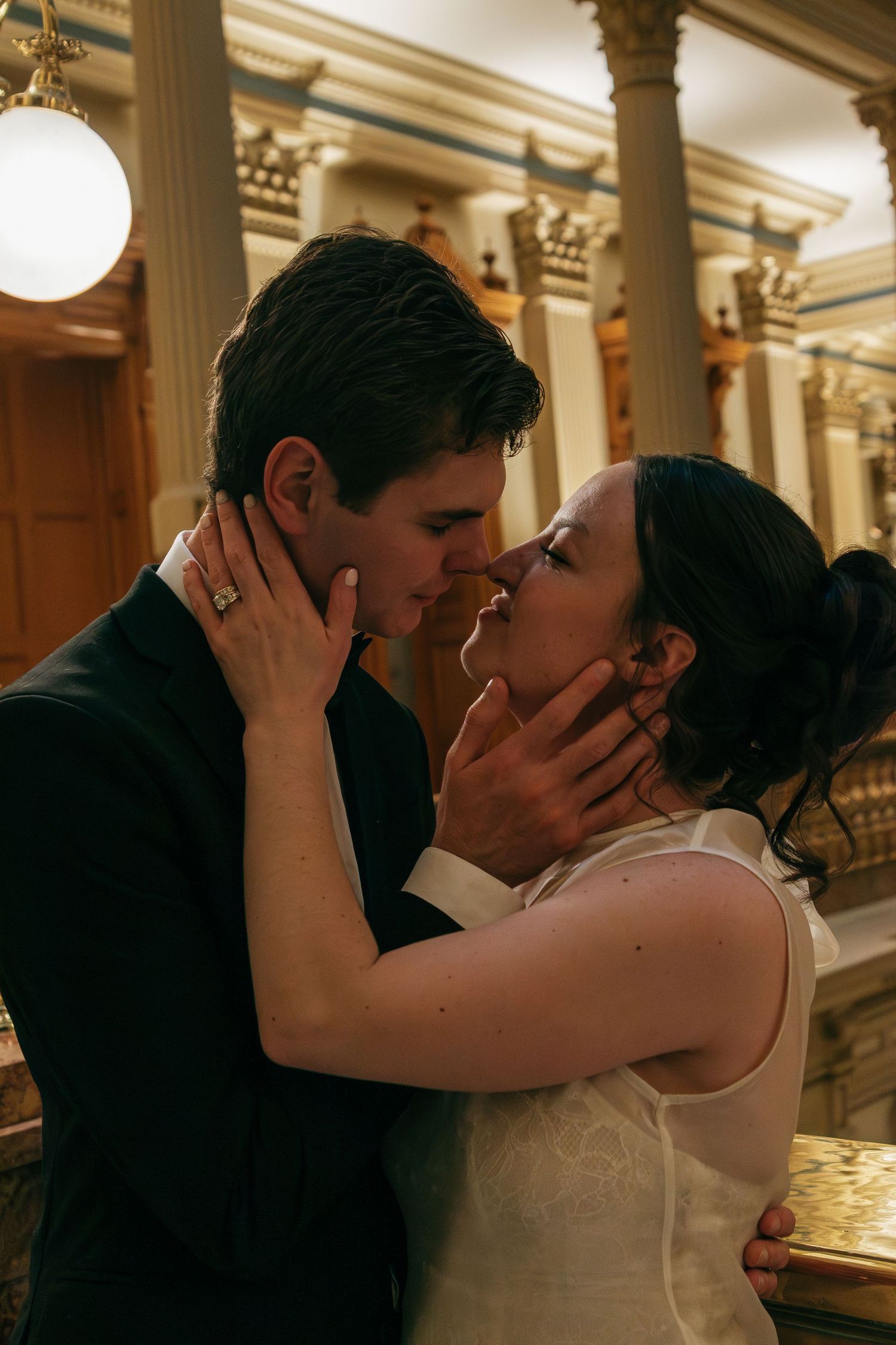 A passionate wedding moment captured in warm lighting with classical architecture in the background.