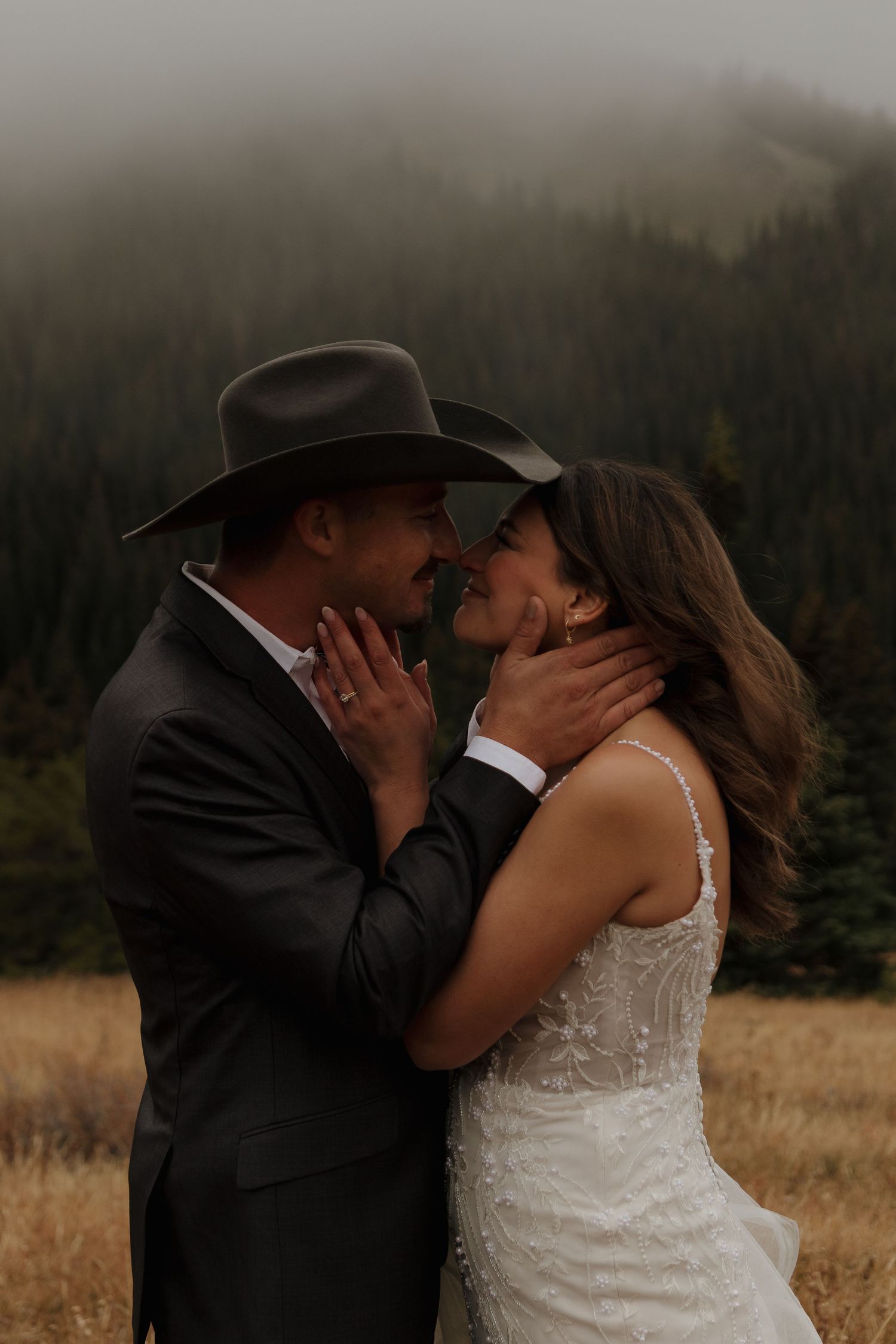 A romantic moment captured between a couple in wedding attire against a moody mountain backdrop.