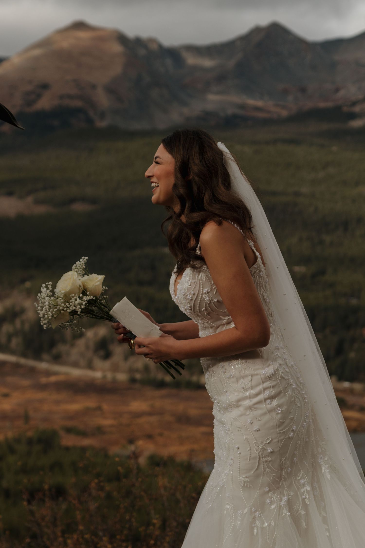 A bride reads from a paper against a backdrop of mountain vistas.