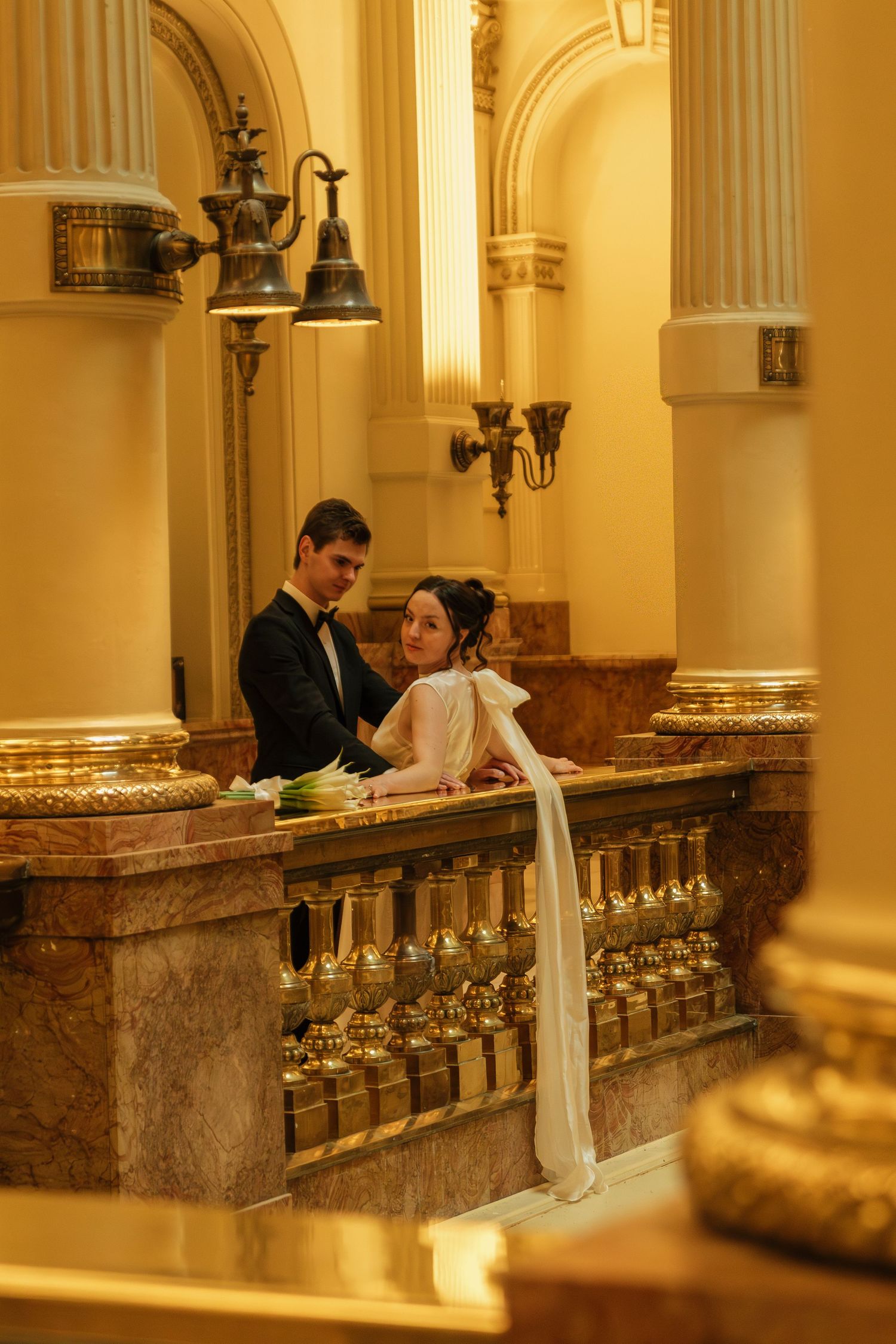 Wedding couple in elegant hallway with ornate marble columns and warm lighting.