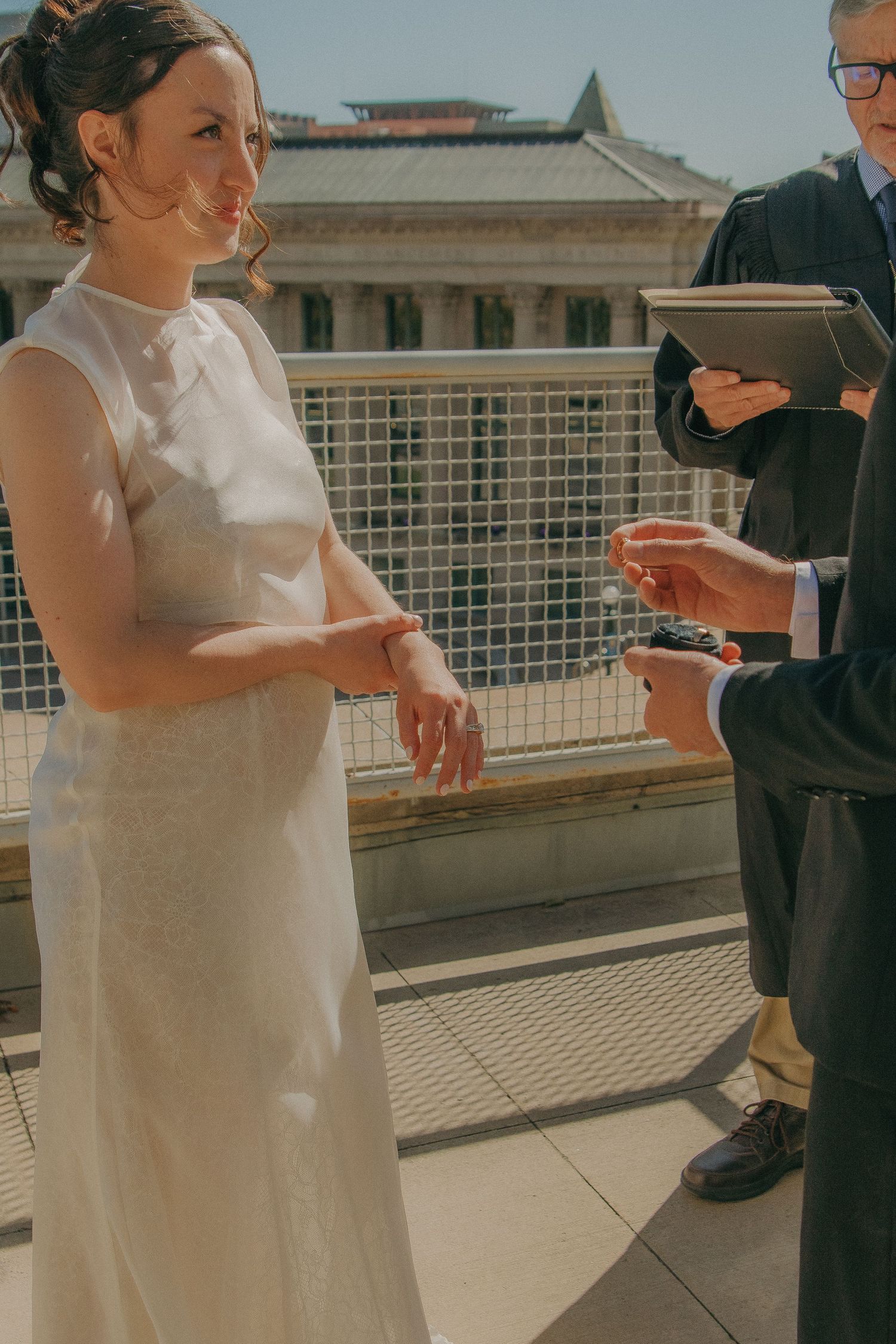 Wedding ceremony taking place on a sunny rooftop terrace with urban architecture in the background.