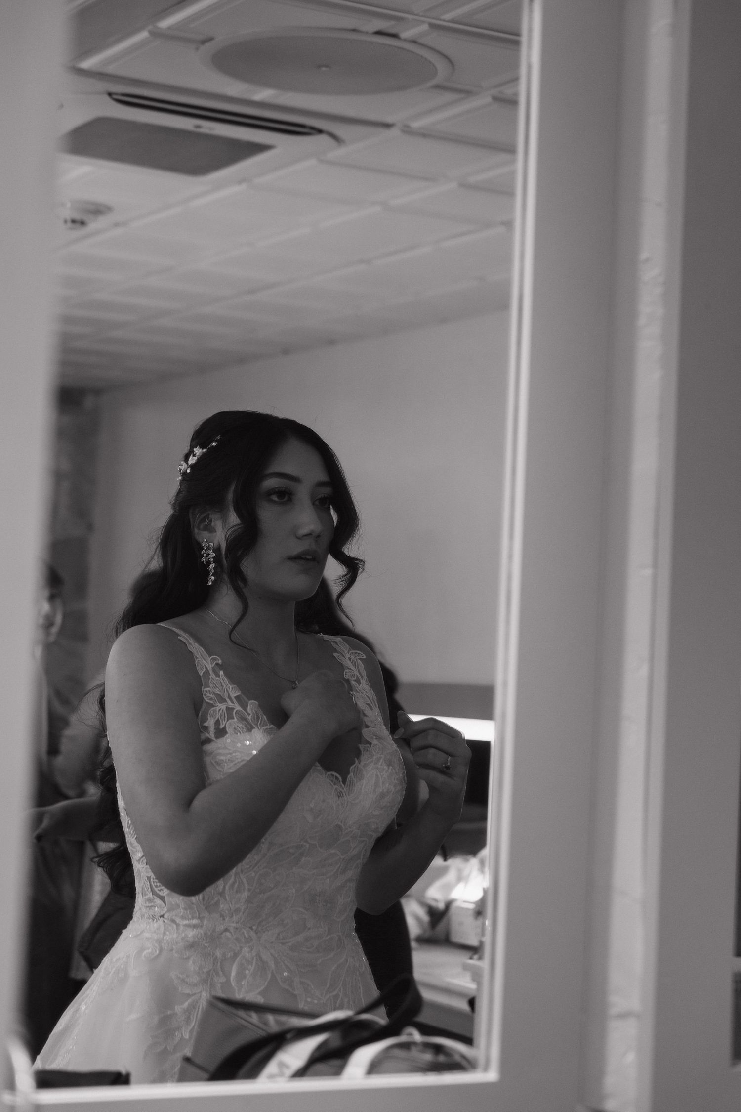Black and white mirror reflection of bride in lace wedding dress getting ready.