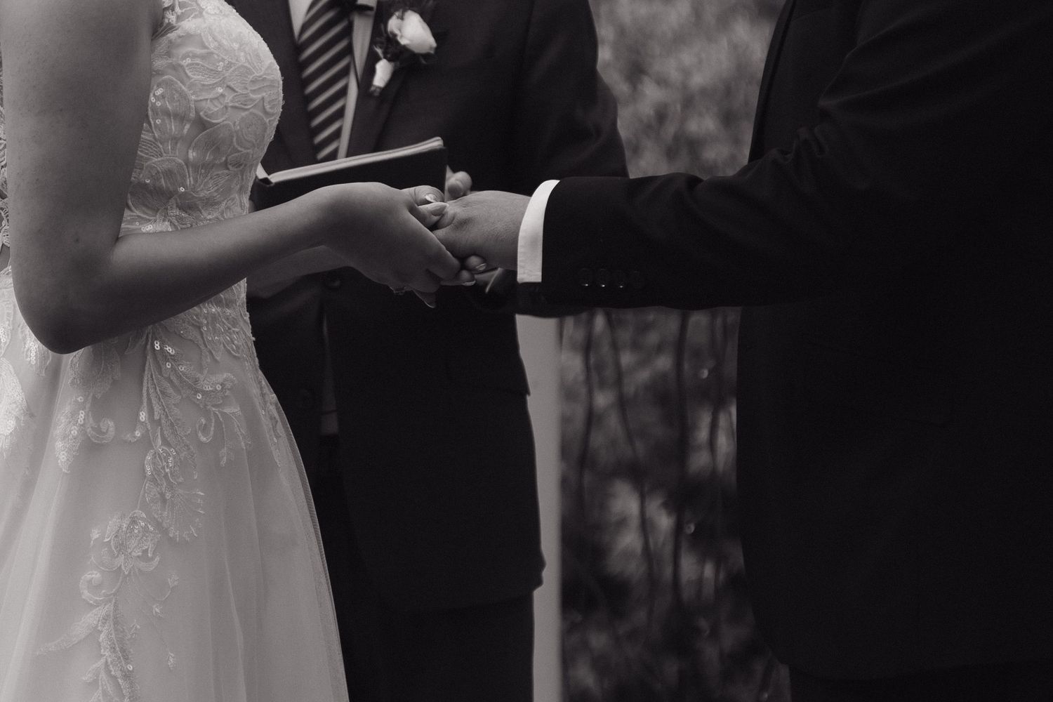 Black and white close-up of bride and groom holding hands during their outdoor wedding ceremony.
