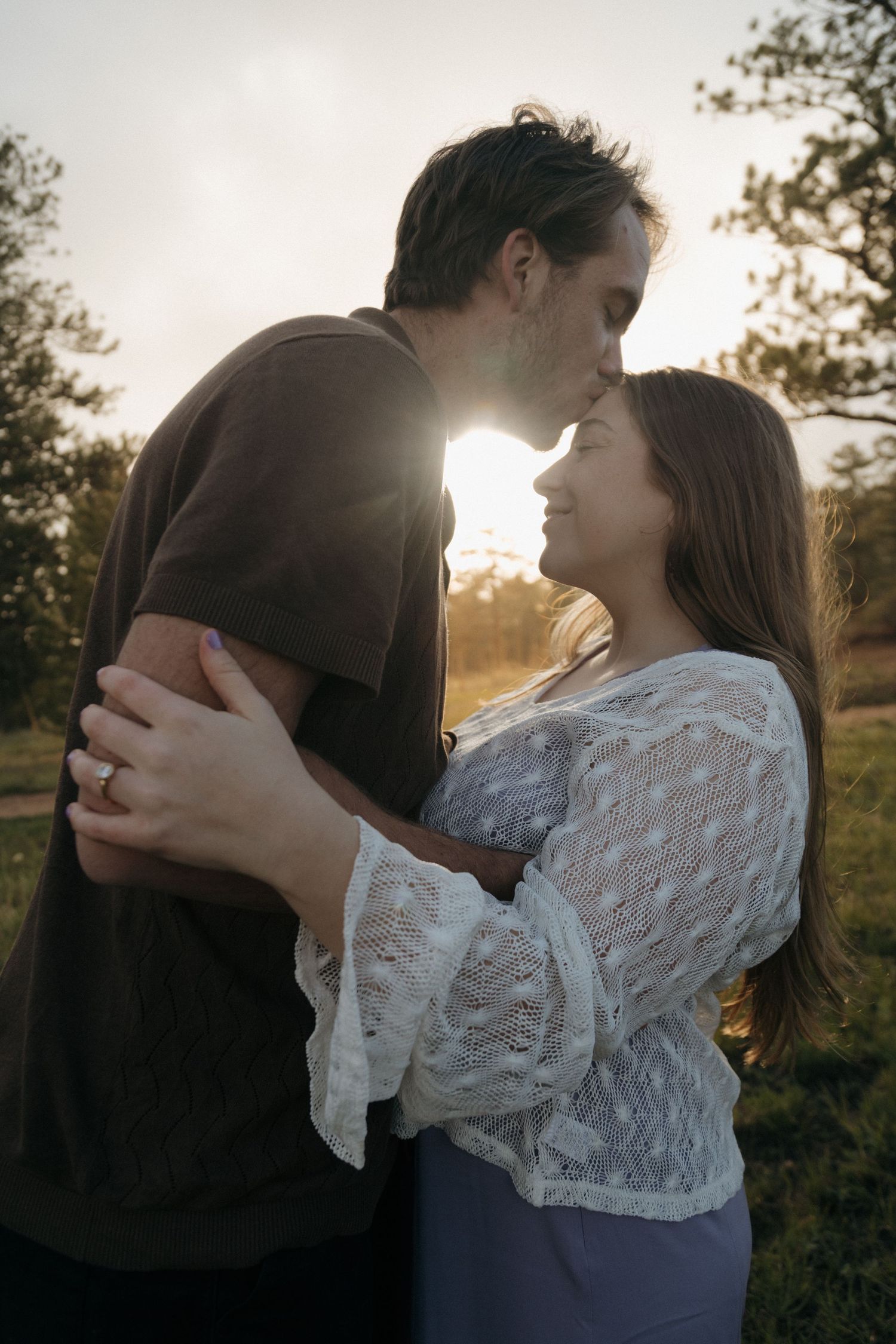 Couple sharing a romantic moment with golden sunset backlight in a scenic outdoor setting.