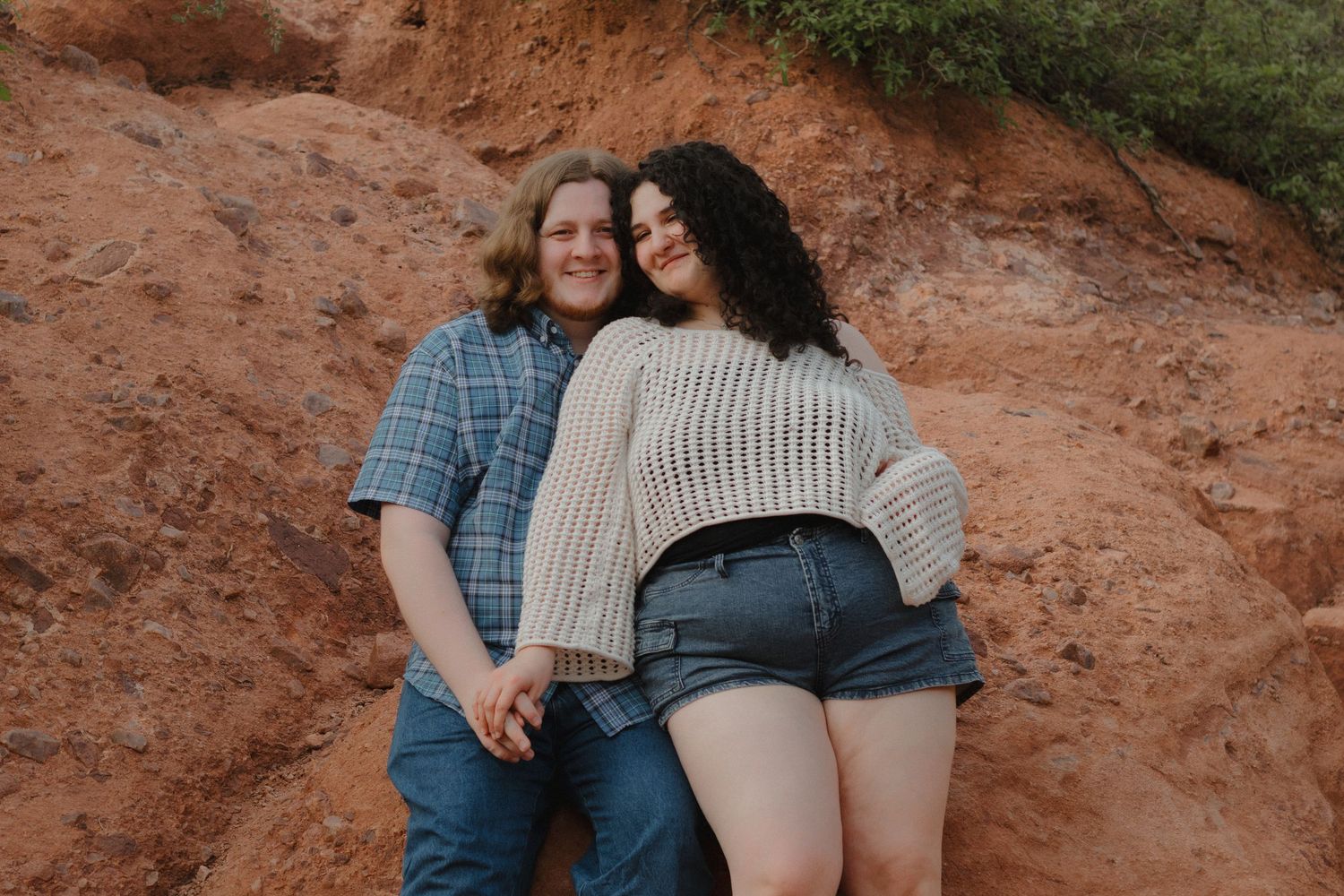 A couple poses casually against a red rock formation in nature.
