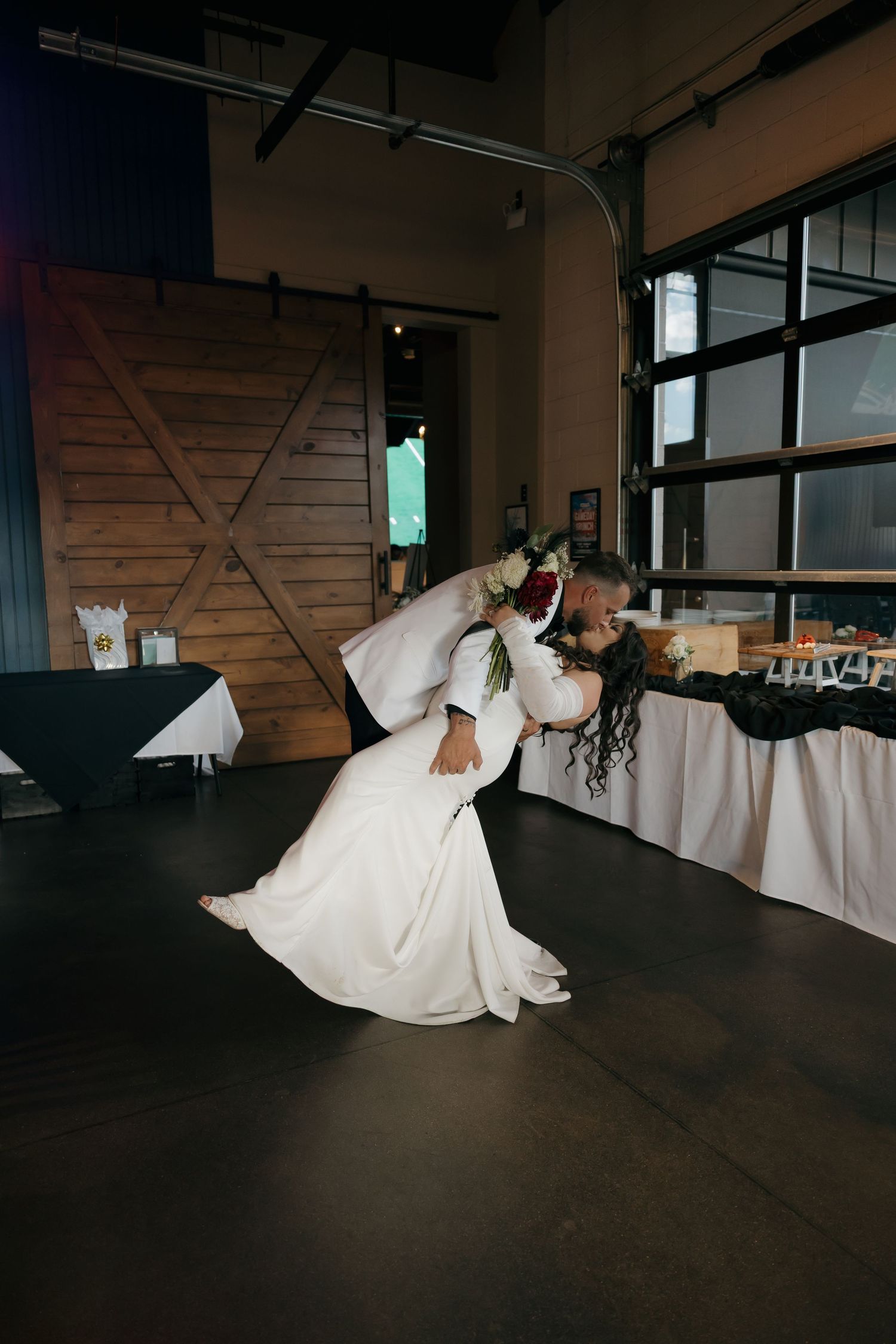Groom dramatically dips bride during first dance at rustic wedding reception venue.