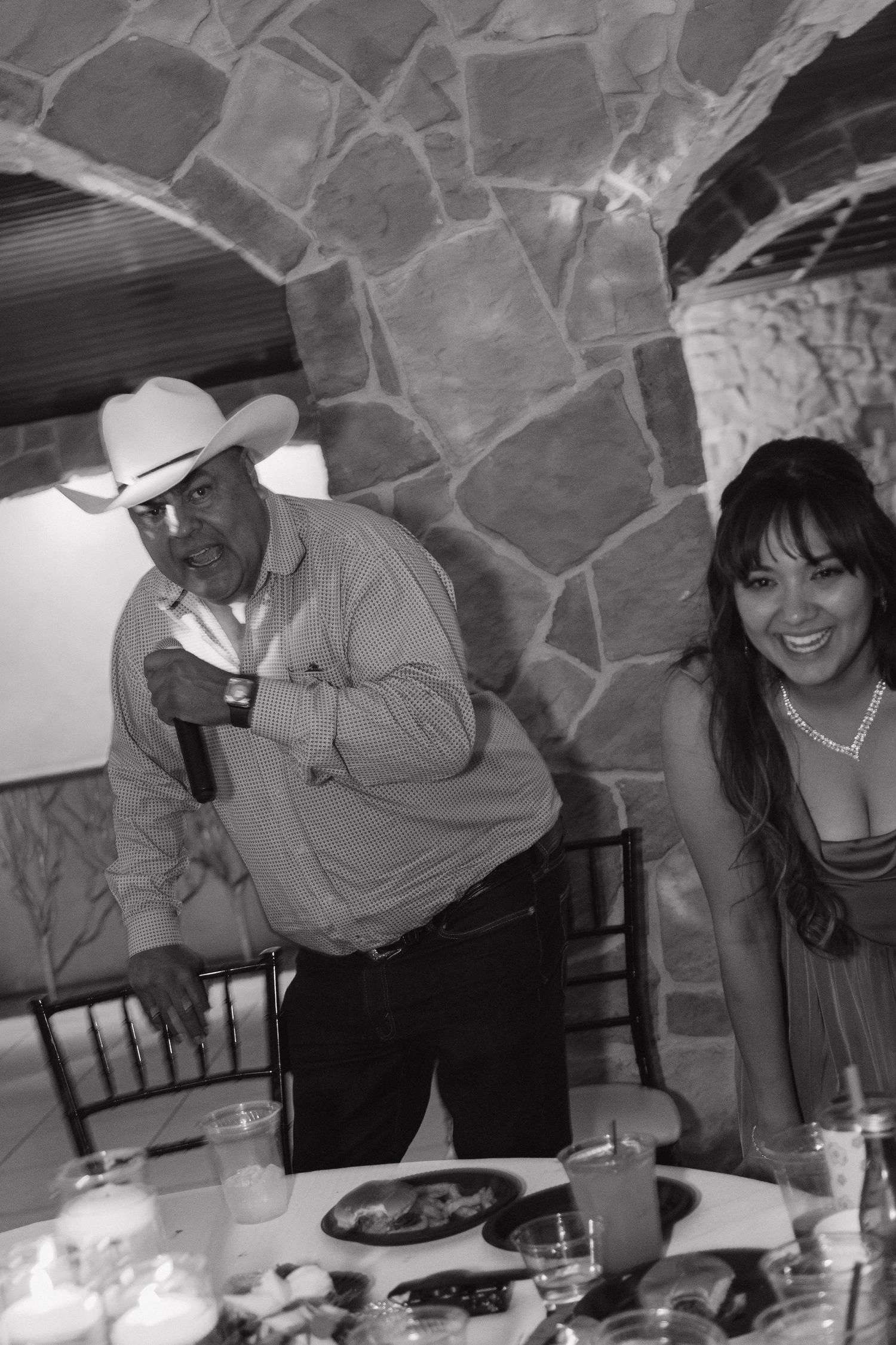 Black and white photo of man in cowboy hat and smiling woman at wedding reception table.