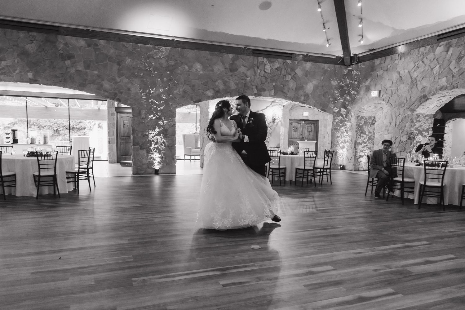 Bride and groom share their first dance in elegant stone-walled wedding reception hall.