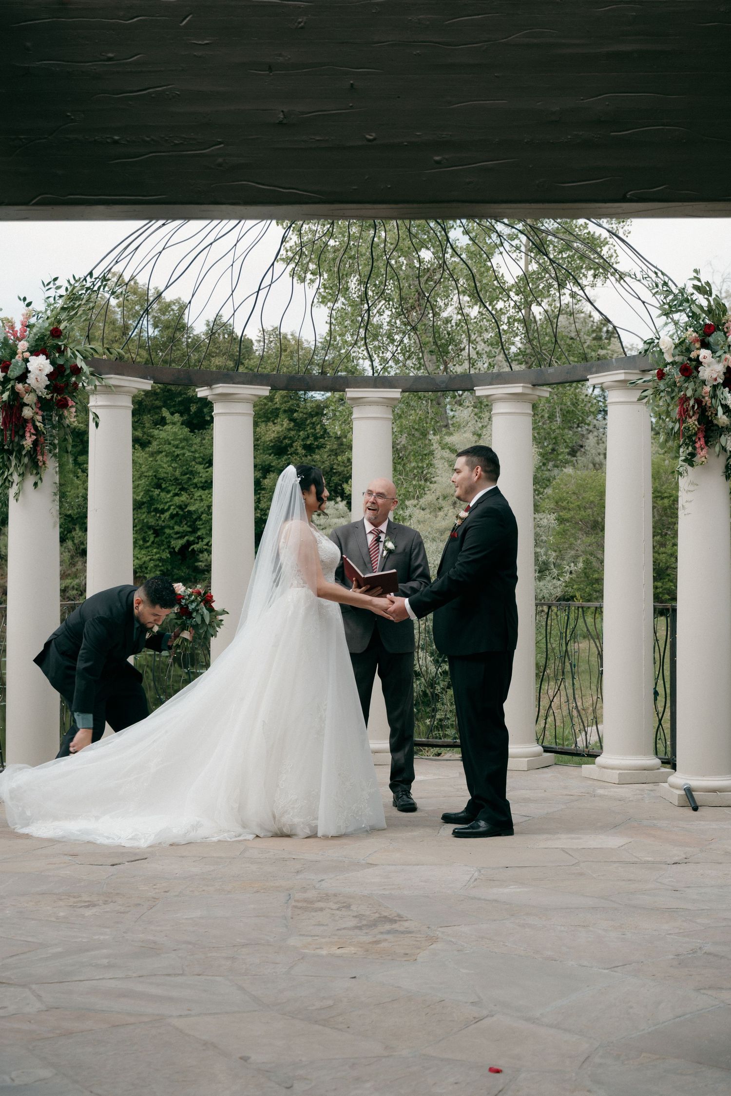 Bride and groom exchange vows at elegant outdoor ceremony with white columns and floral arch.