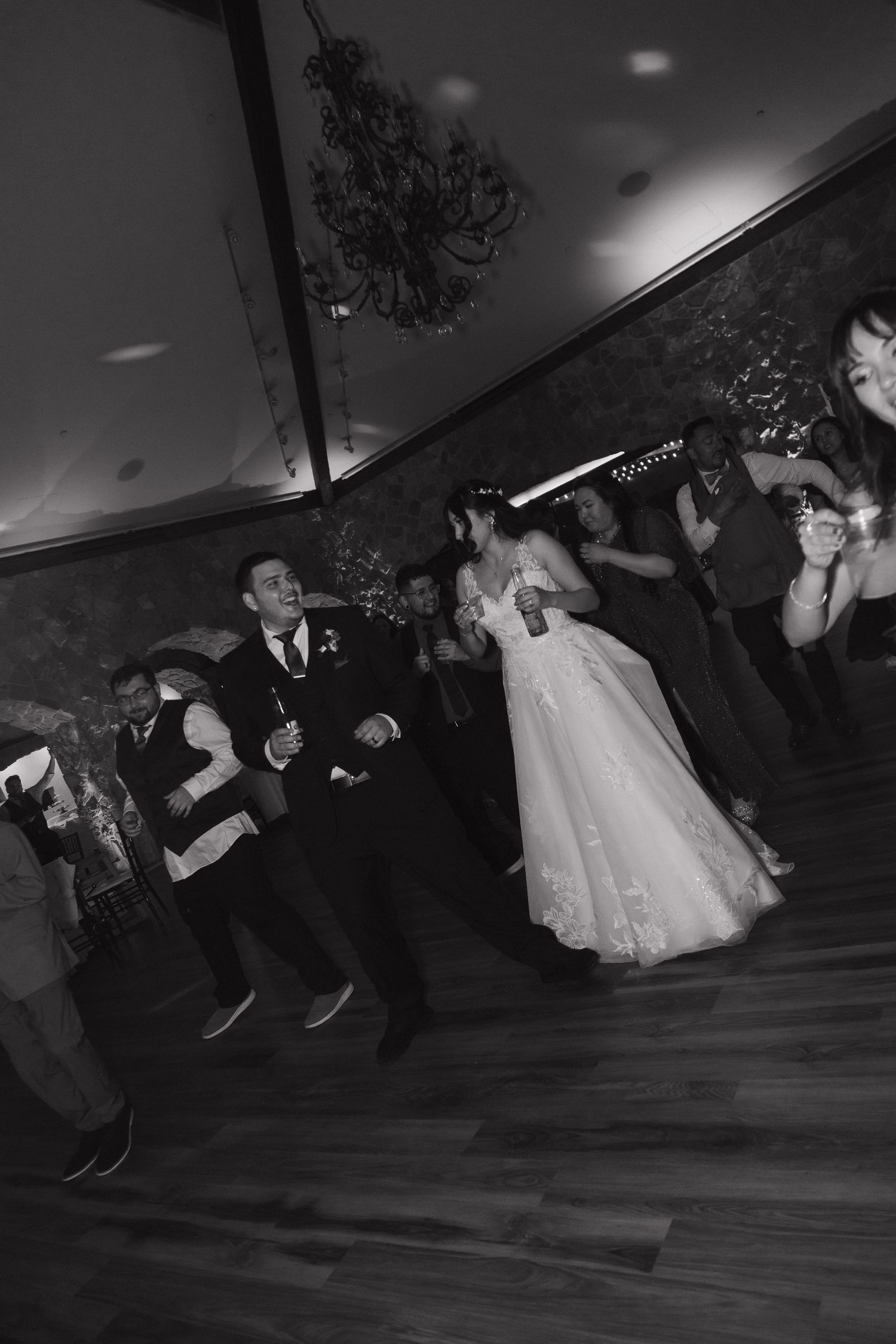 Bride and groom dancing joyfully surrounded by celebrating guests on the wedding reception dance floor.