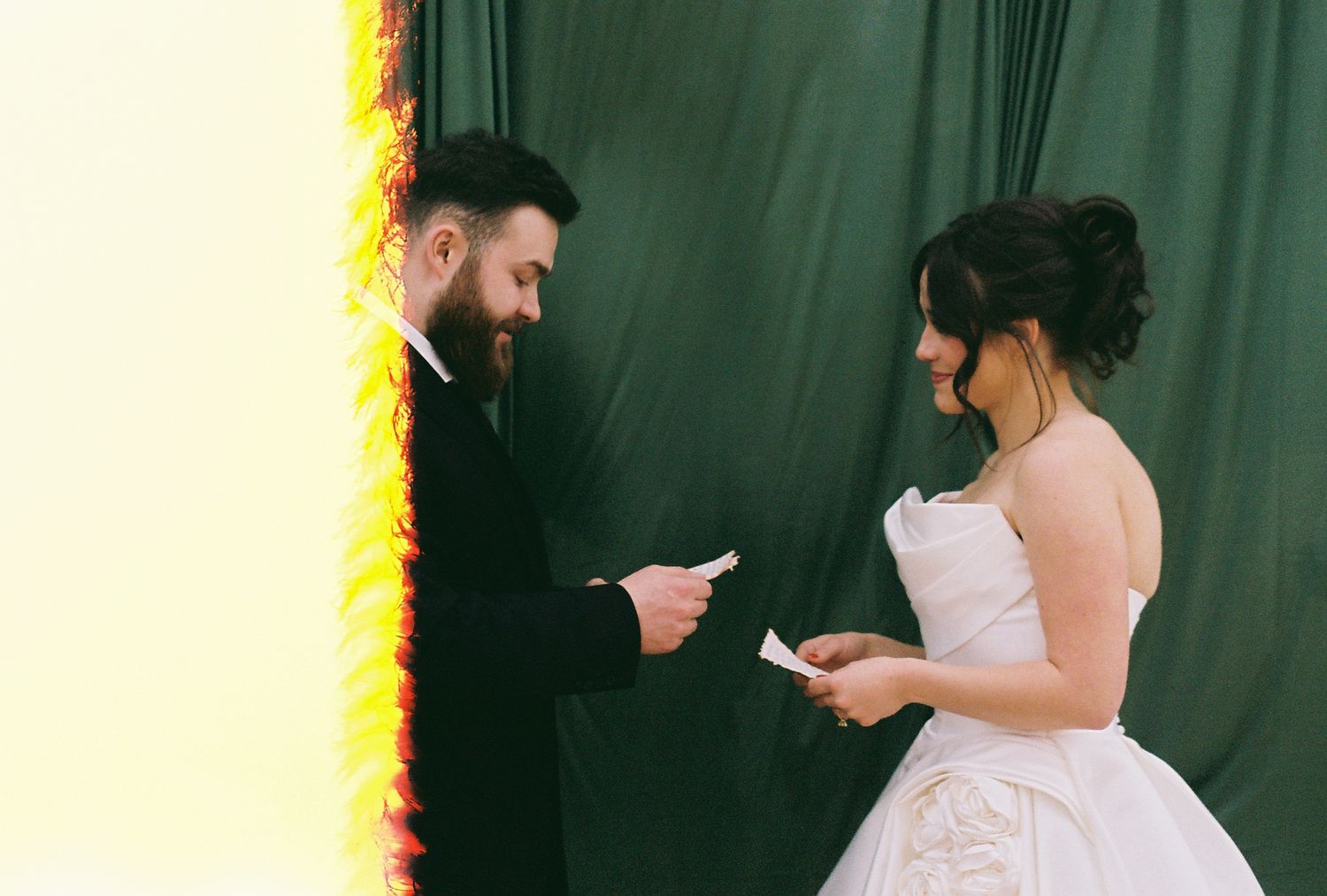 A couple exchanging vows against a green backdrop with warm lighting.