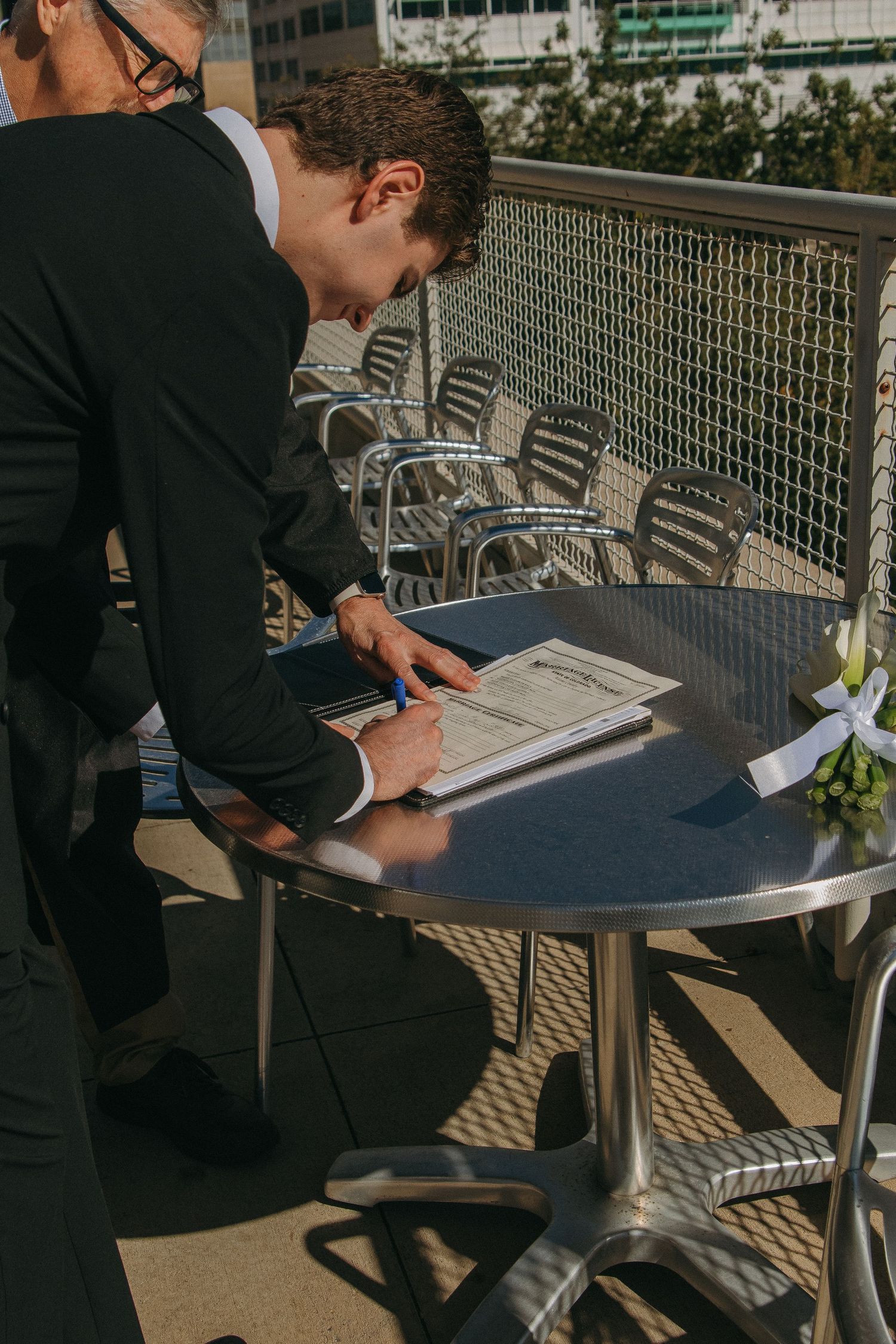 Someone in formal attire signing documents at an outdoor table.