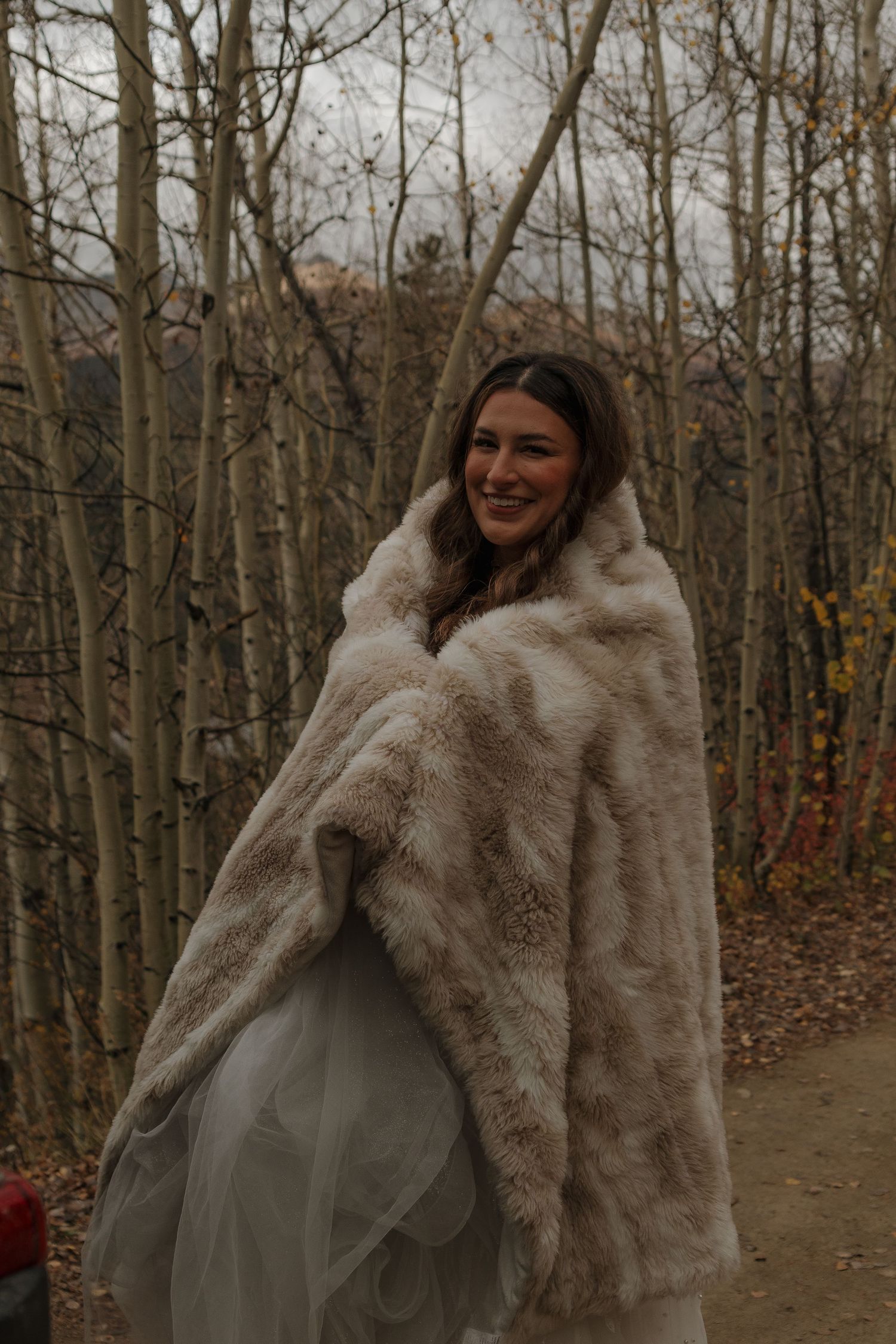 A winter bride wearing a cozy fur jacket over her wedding dress in a forest setting.