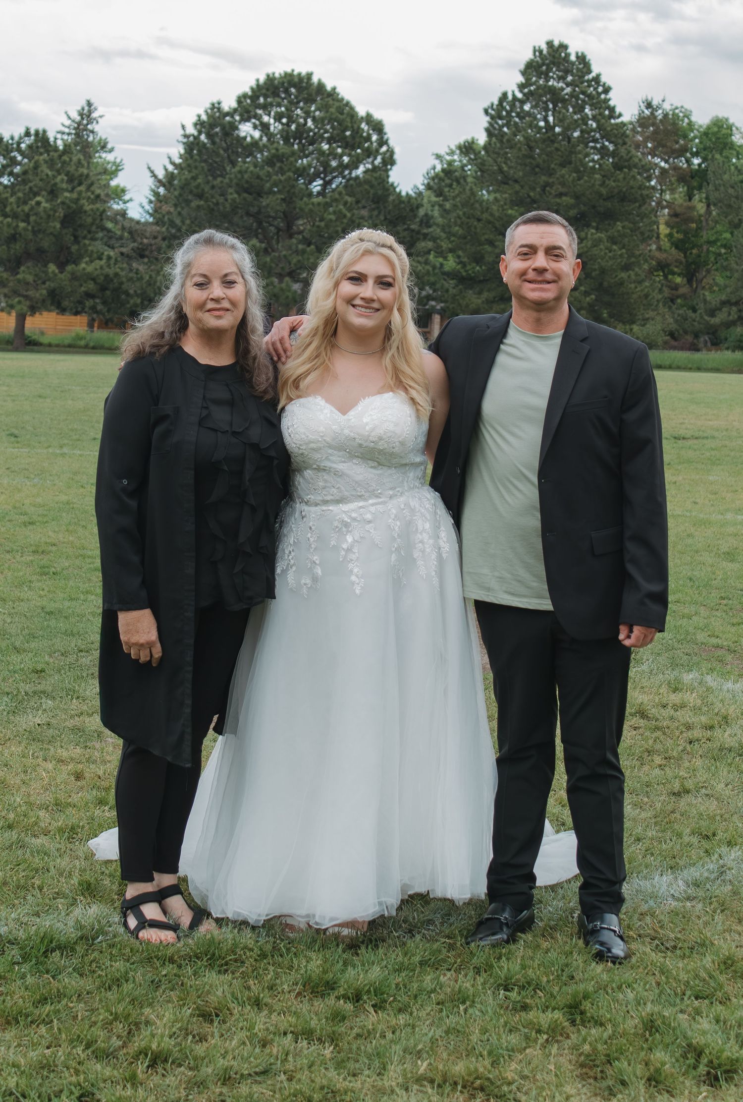 Wedding party group photo with bride in white dress on grass field.
