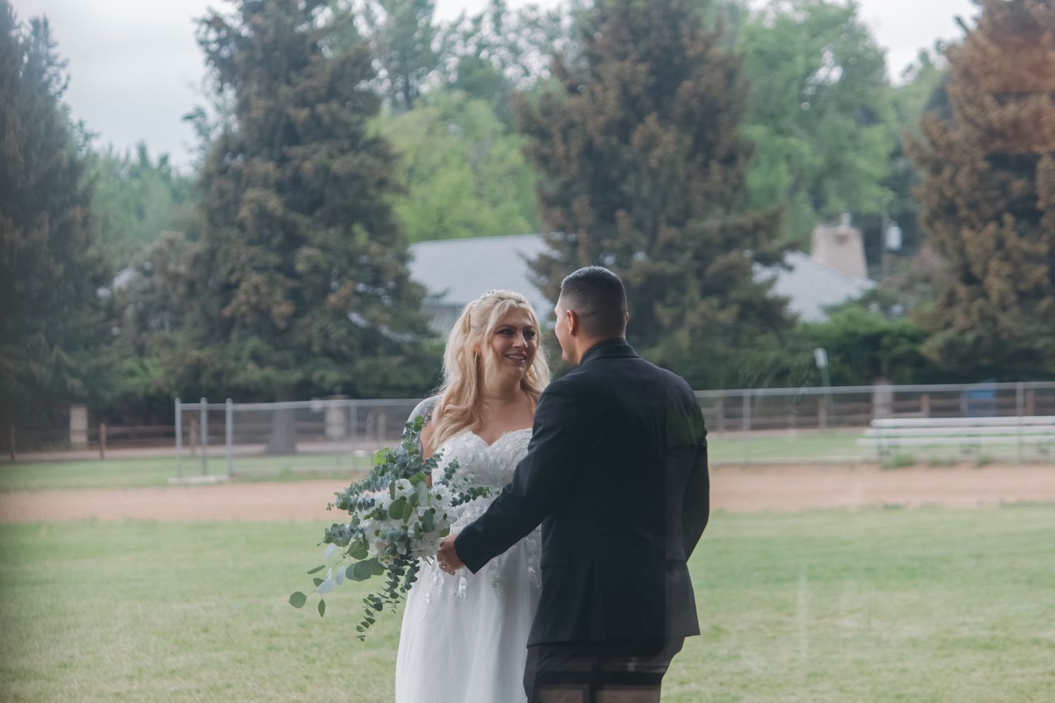 Panoramic view of a wedding couple walking through a park with evergreen trees.