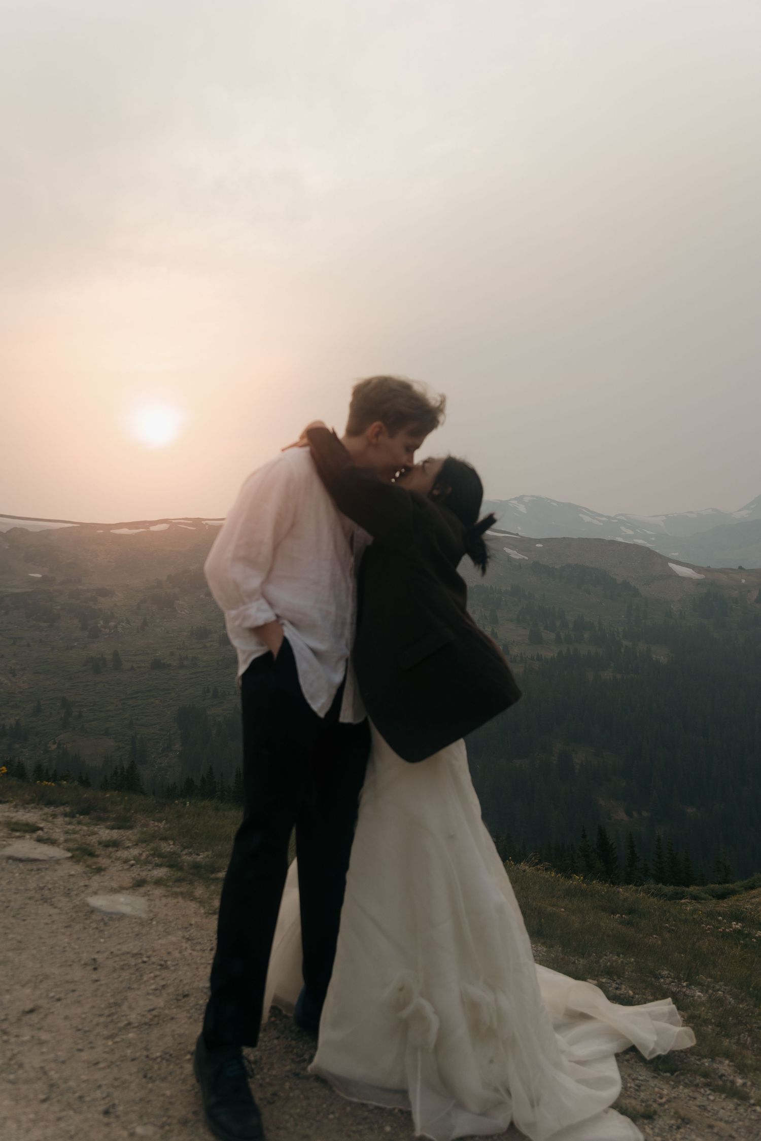 Couple sharing a romantic kiss at sunset on a mountain summit during their outdoor elopement.