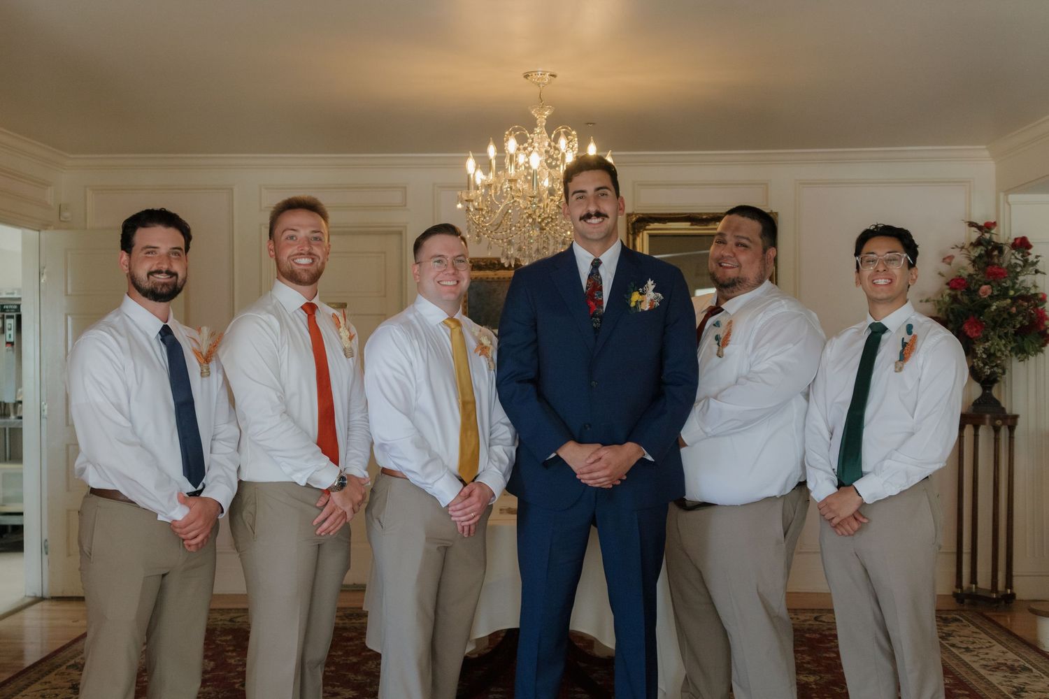 Groomsmen in white shirts and ties posing together in an elegant room with chandelier.