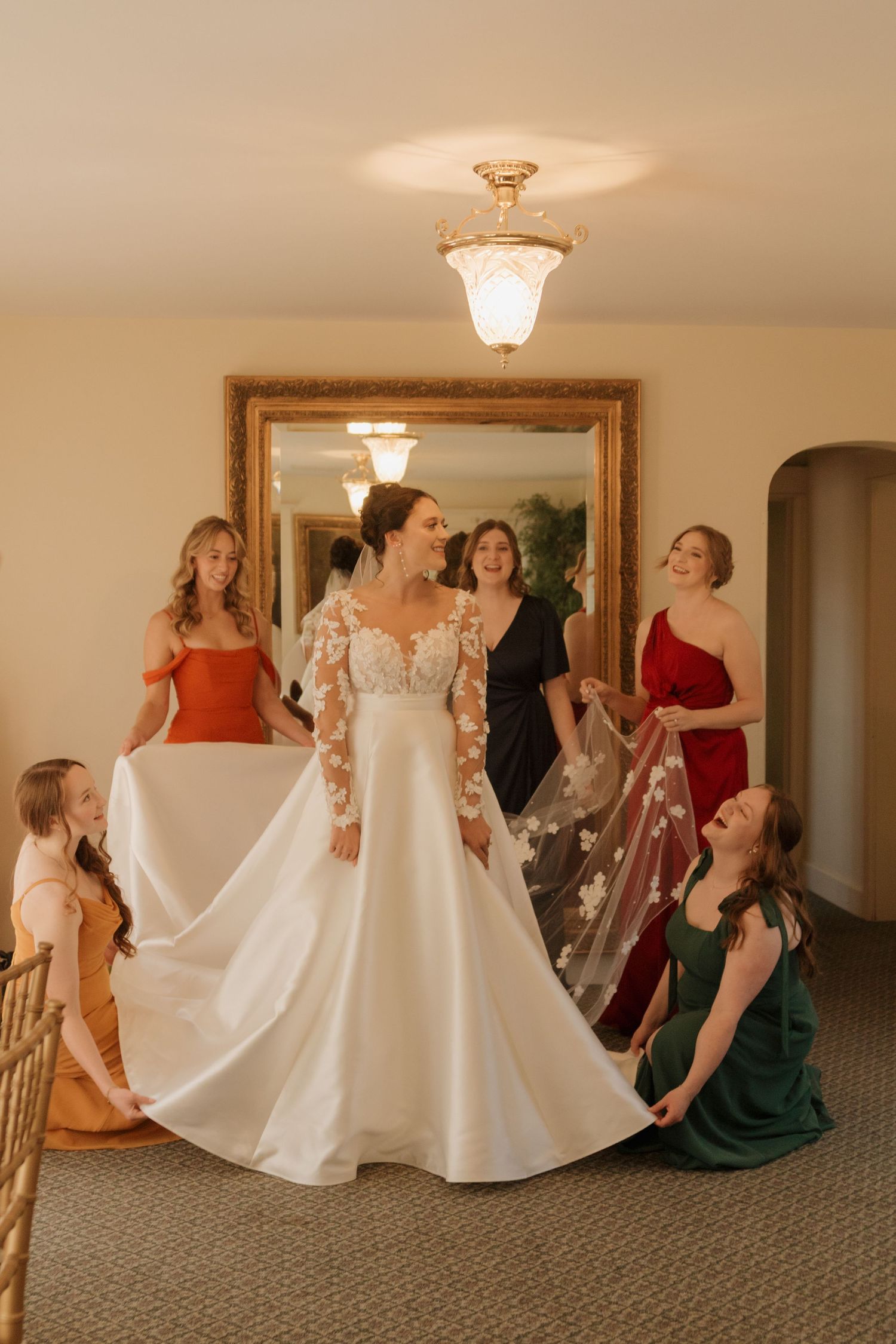 Wedding party helping bride with large white dress skirt in elegant indoor setting.