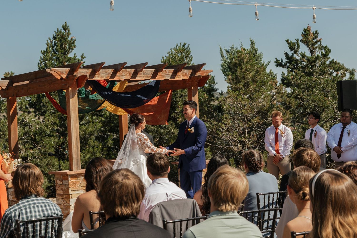 Wedding ceremony progression under rustic wooden pergola with string lights and blue sky.