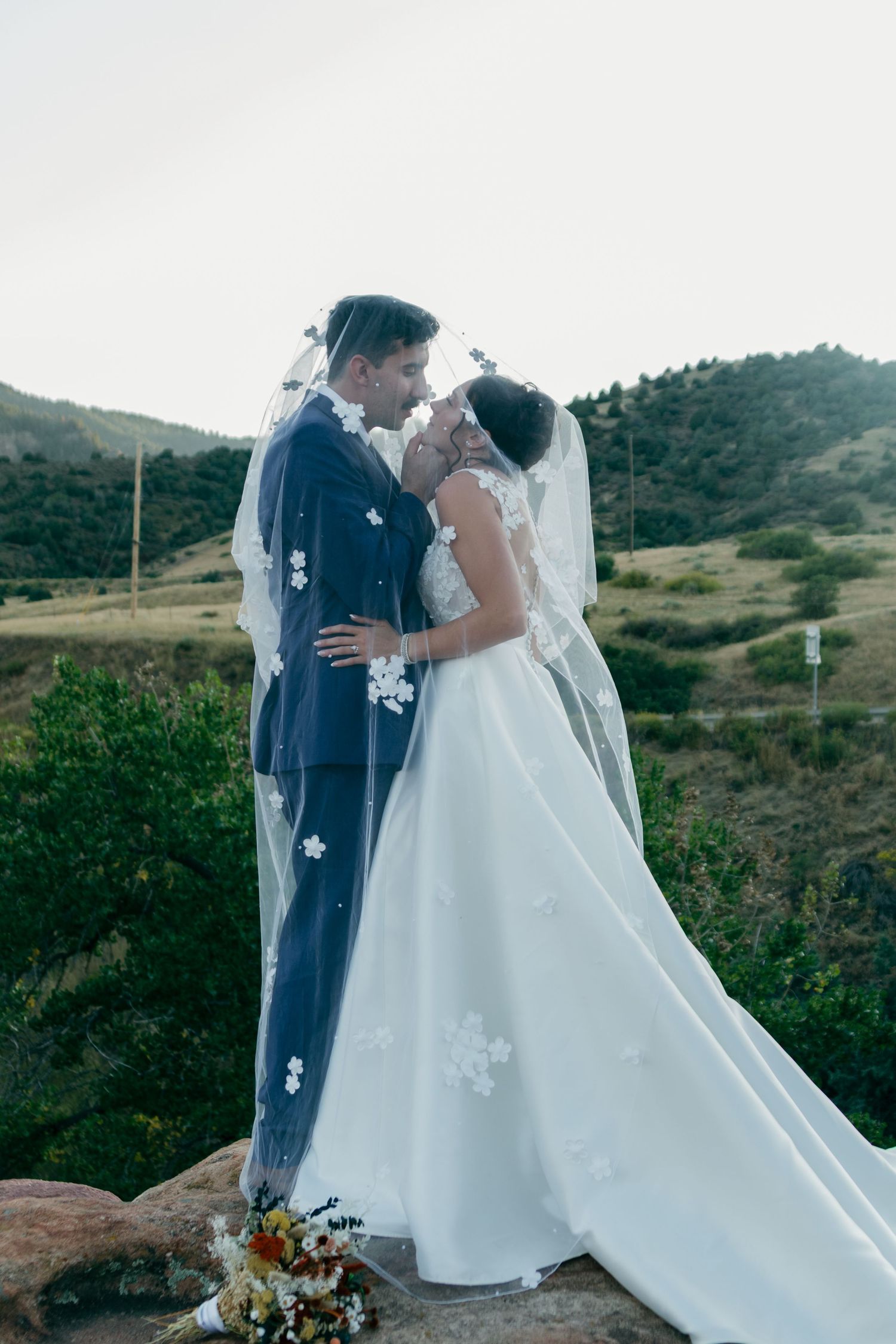 A couple sharing a romantic moment in their wedding attire against a mountainous backdrop.